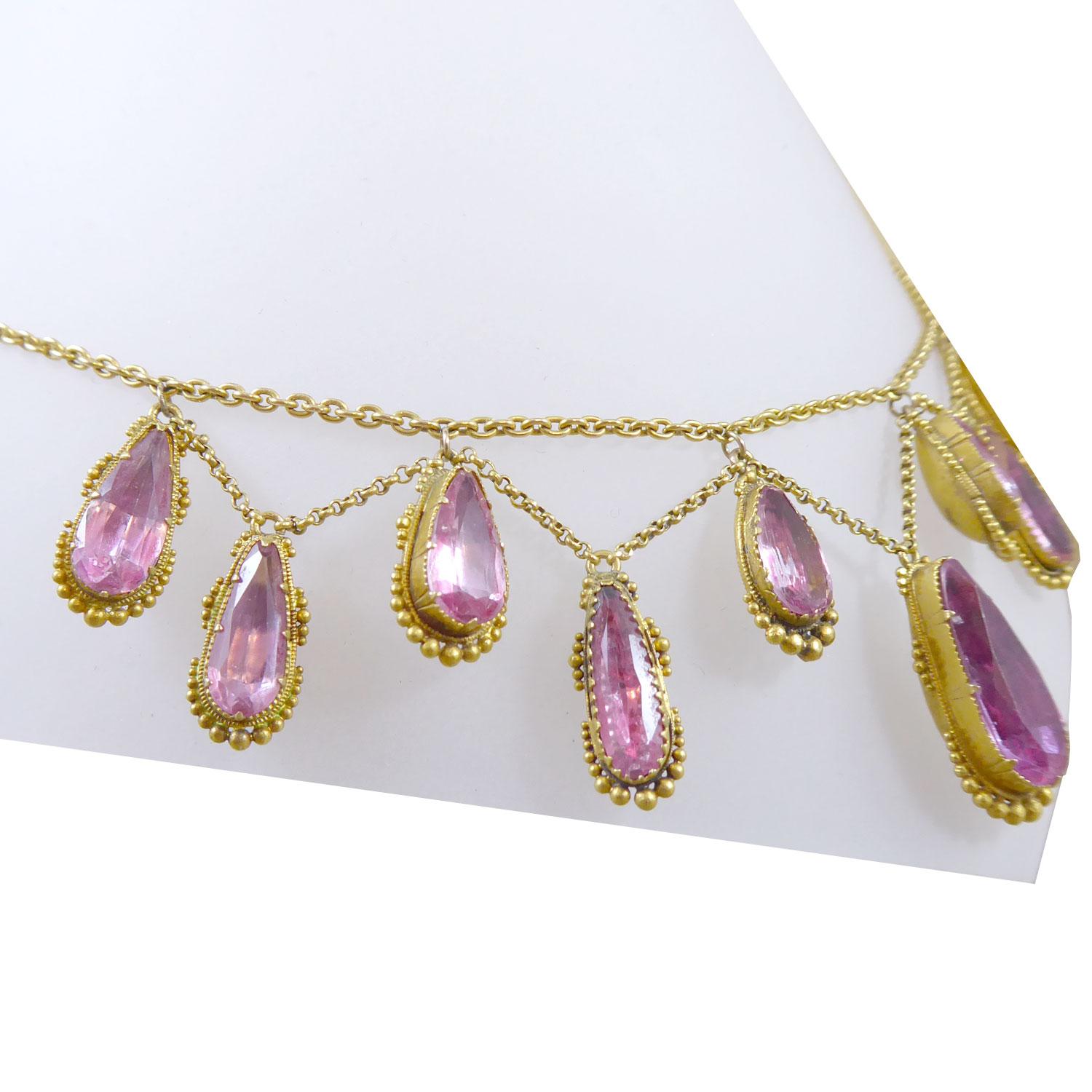 A delightful antique necklace created circa 1850 and comprising a fringe of pear shaped, foil-backed pink topaz in claw settings with granulatiion detailed border.  The topaz, 11 in total, suspend from yellow trace chain in a garland/swag design