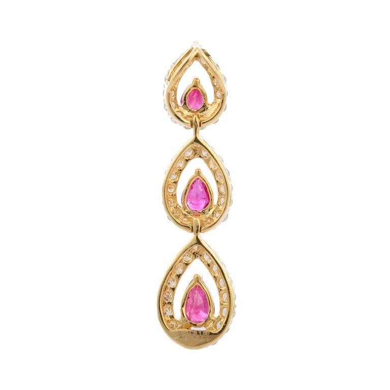 Réalisé en luxueux or jaune 18 carats, ce superbe pendentif met en valeur un gracieux trio de rubis en forme de poire totalisant 1,00 carat. Chaque rubis est délicatement encadré par un halo de diamants ronds de taille brillant, pour un poids total