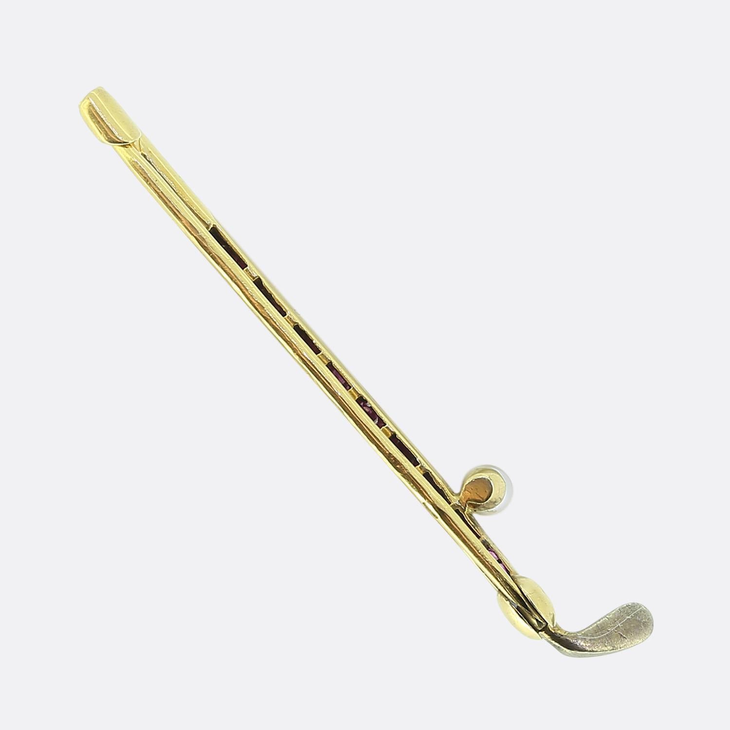 Here we have a playful brooch dating back the Edwardian period. Crafted from a warm 18ct yellow gold, this brooch takes on the form of a golf club. The shaft is adorned with square calibre cut pink rubies, adding a touch of vibrancy. A round white