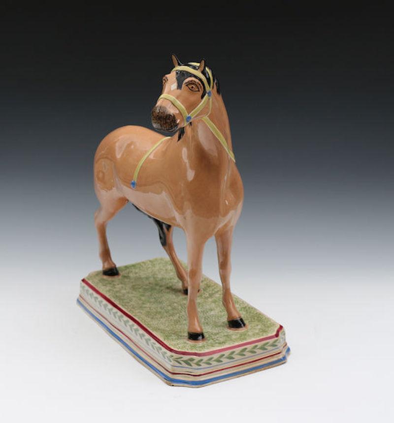Dated: 1810 to 1820 Leeds Yorkshire England

A rare large scale pottery pearlware figure of a horse standing square on a green sponged decorated oblong base with maroon and blue stripes. The horse is wearing a yellow bridle with blue terminals.