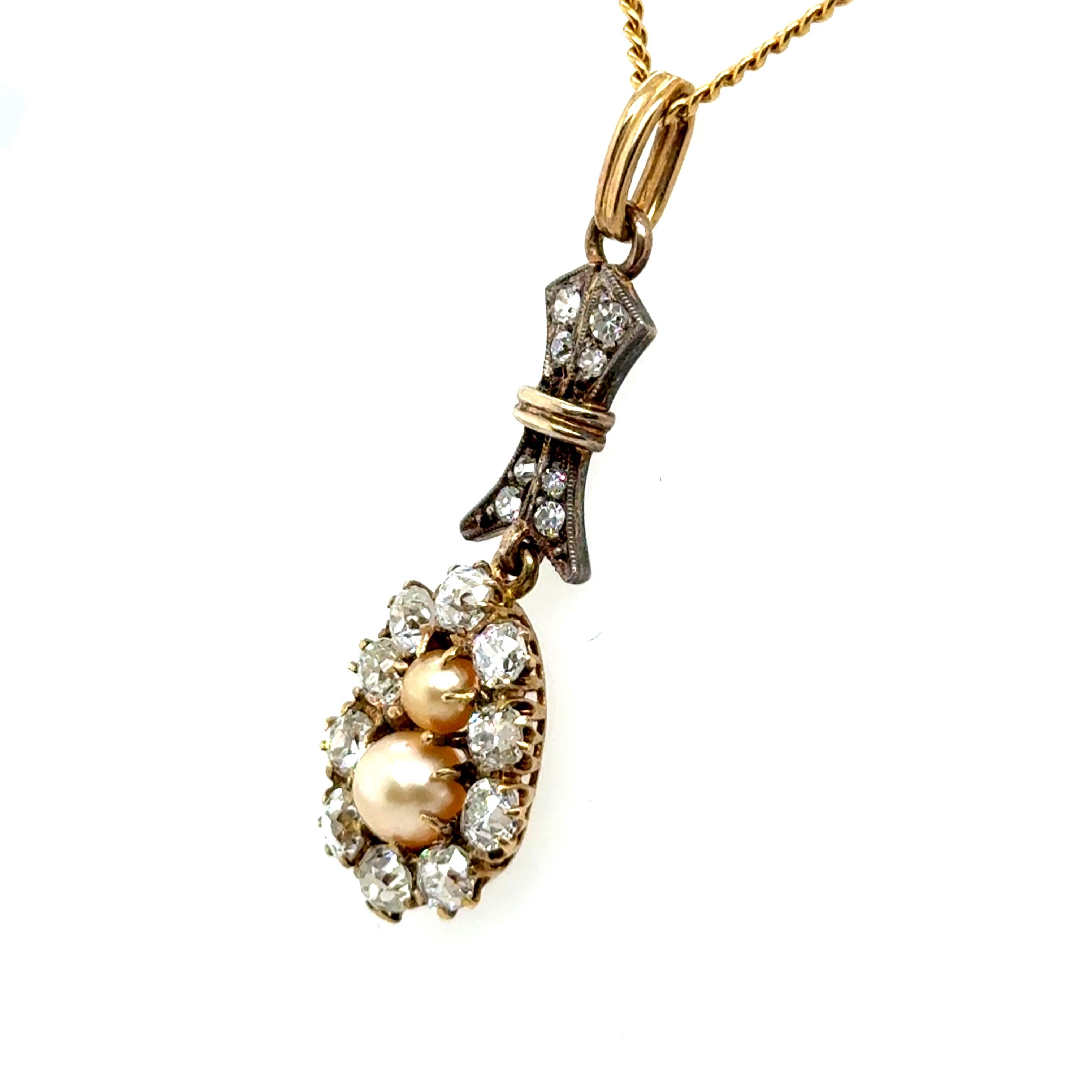 This antique pendant is crafted in 18-karat yellow gold with silver accents, exuding vintage charm. It features two natural pearls elegantly nestled at the center, surrounded by a halo of ten old-cut diamonds totaling 1.20 carats in G-H color and