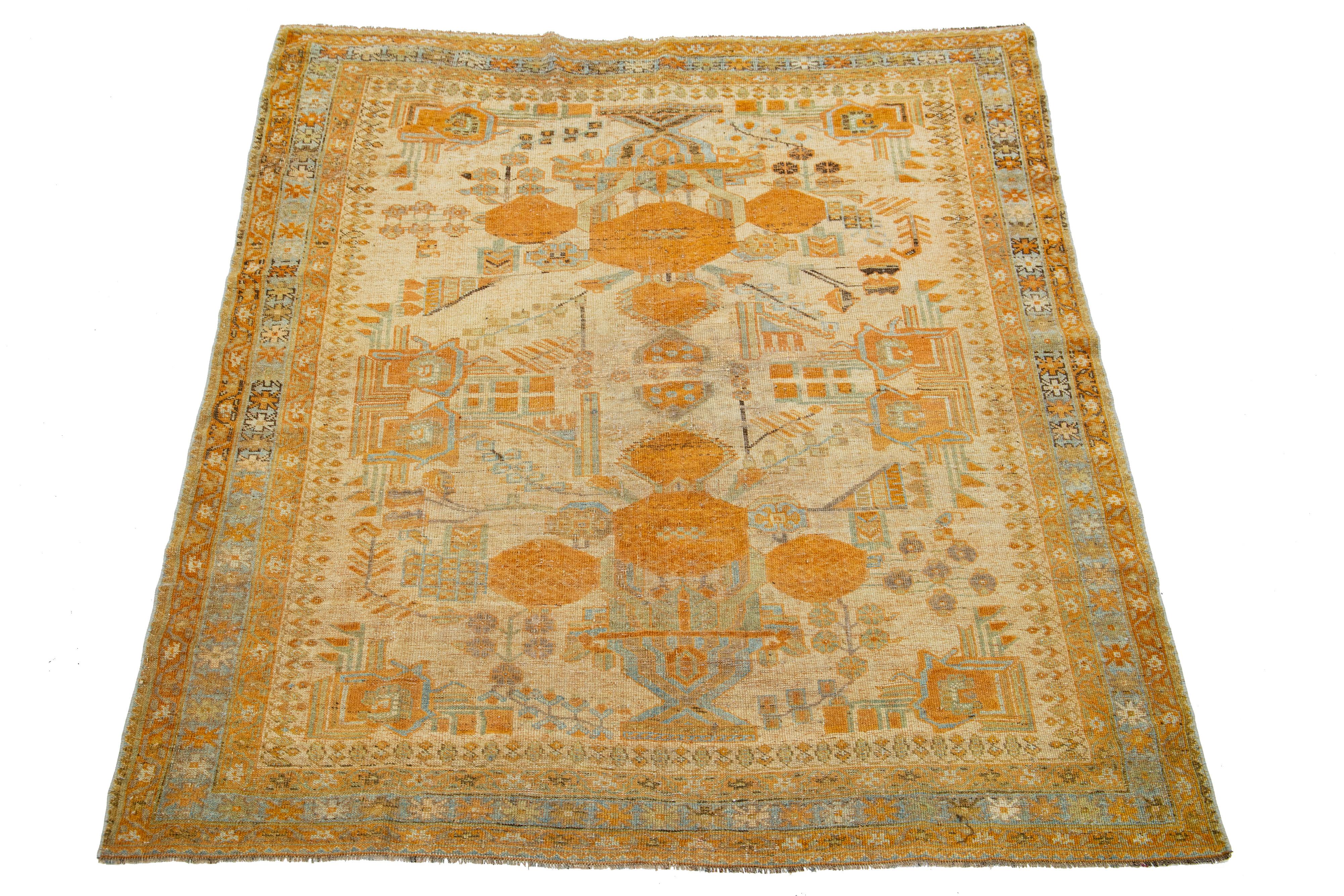 Beautiful antique Persian hand-knotted wool rug with a tan color field. This piece has a blue-designed frame with orange accents in a gorgeous all-over pattern.

This rug measures 5' x 6'1