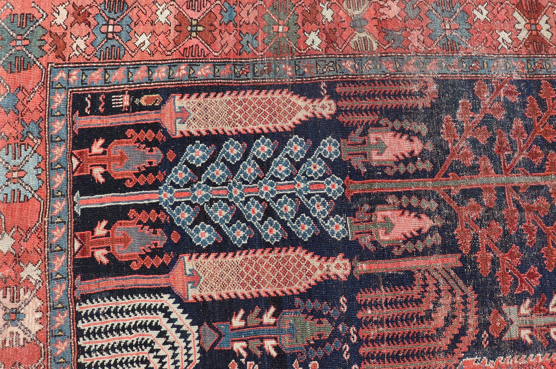 This antique Persian Bakhshaish rug features an all-over tree design with willow trees, branches and leaves displaying a variety of garden trees. Set upon a Navy background the colorful field and border include brick red, light blue, salmon, green,