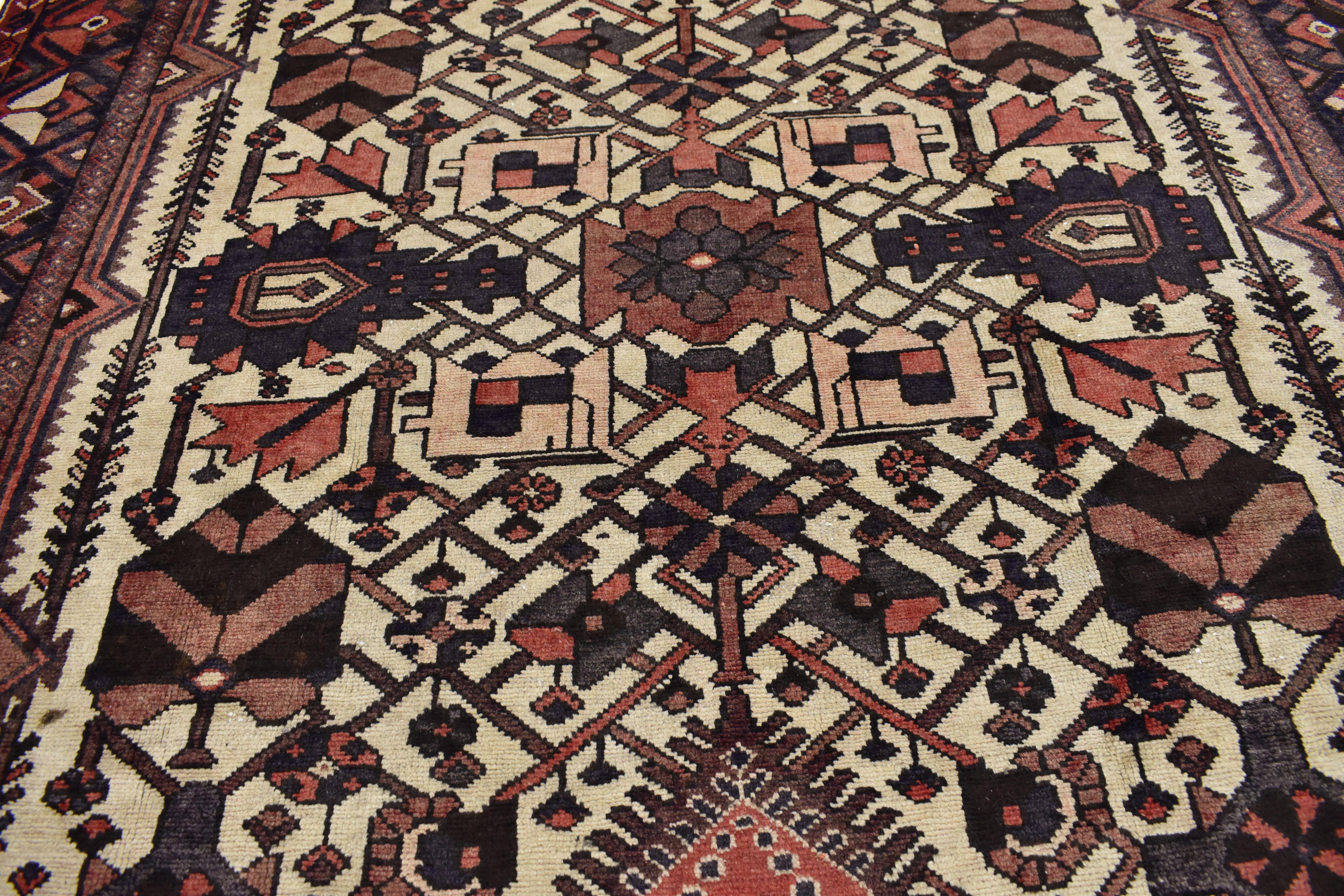 75268, an antique Bakhtiari rug. This hand-knotted wool vintage Persian Bakhtiari rug features a center trapezoidal lozenge with a lattice pattern and interspersed flowers in hues of red-coral, gray and mocha on a field of sand-beige. A lotus flower