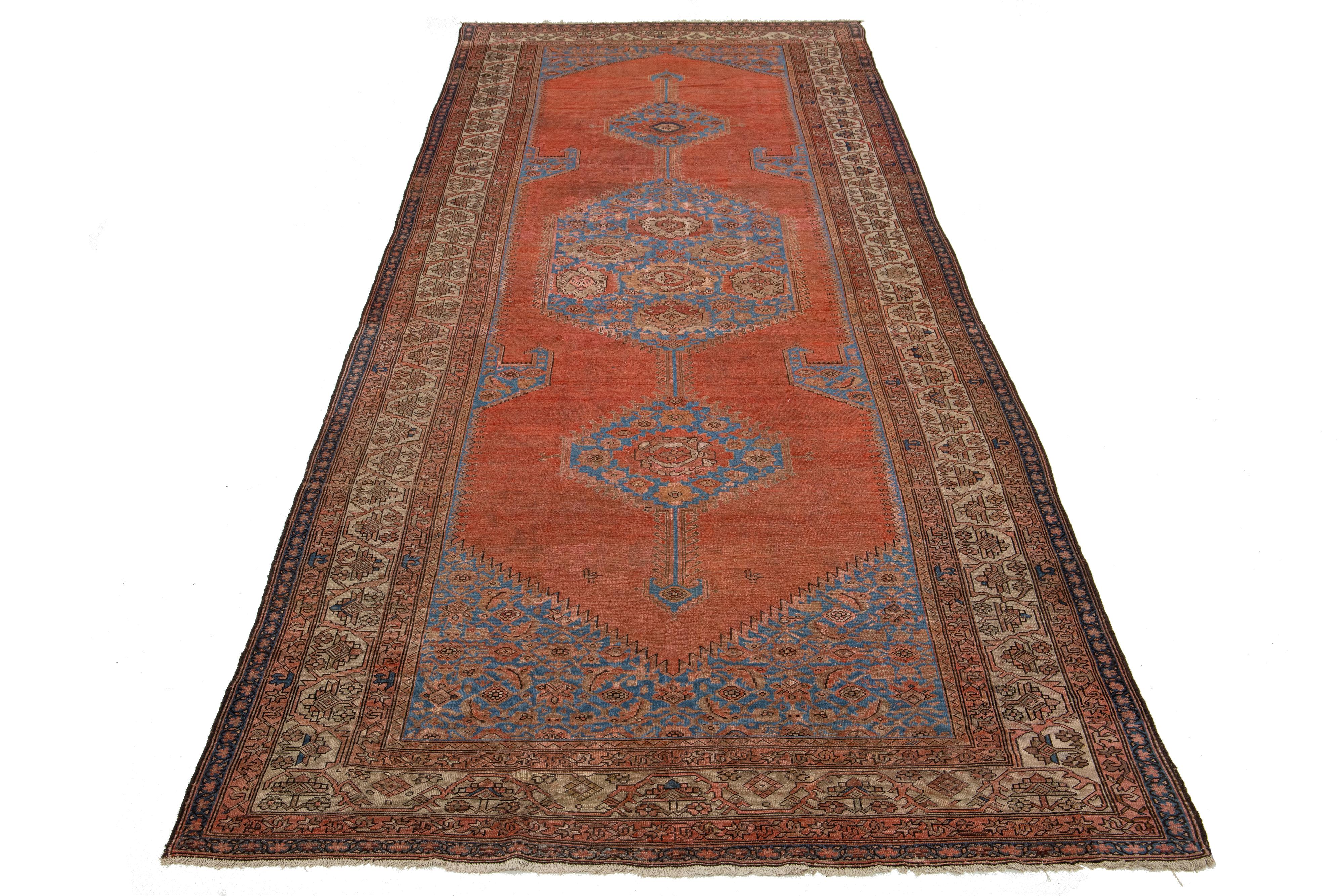 Questo antico runner Bakshaish annodato a mano presenta accenti beige e blu su un vivace sfondo color ruggine. Questi tappeti sono tesori unici per gli intenditori e mostrano motivi distintivi, movimento e asimmetria. L'uso sapiente di tinture