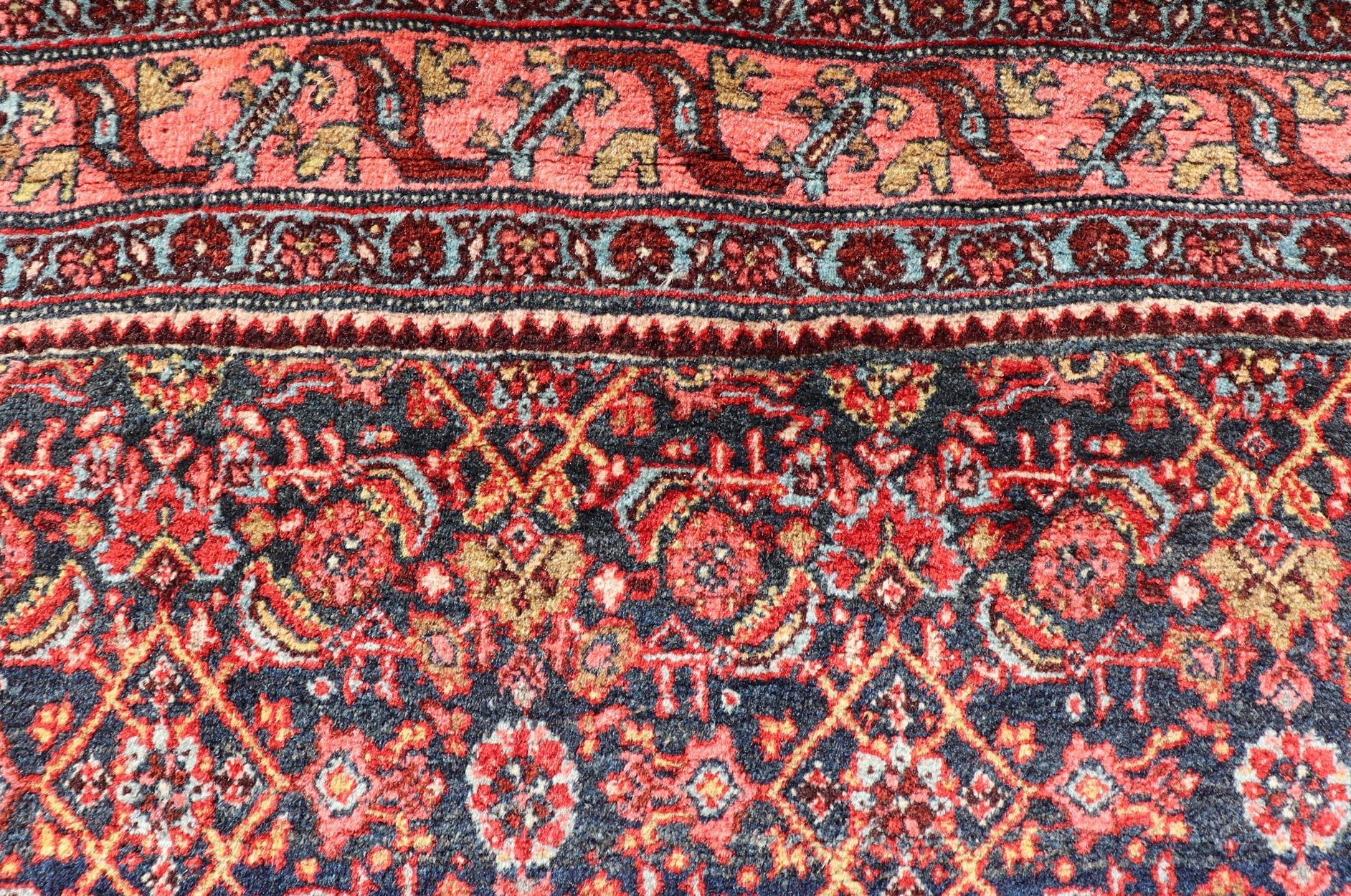 Measures: 4'5 x 6'7 

The rug has a central medallion, surrounded by an intricate floral Herati design. The border utilizes softer colors of pink, blue and yellow to contrast with the background of navy and red-orange design. 

Country of Origin: