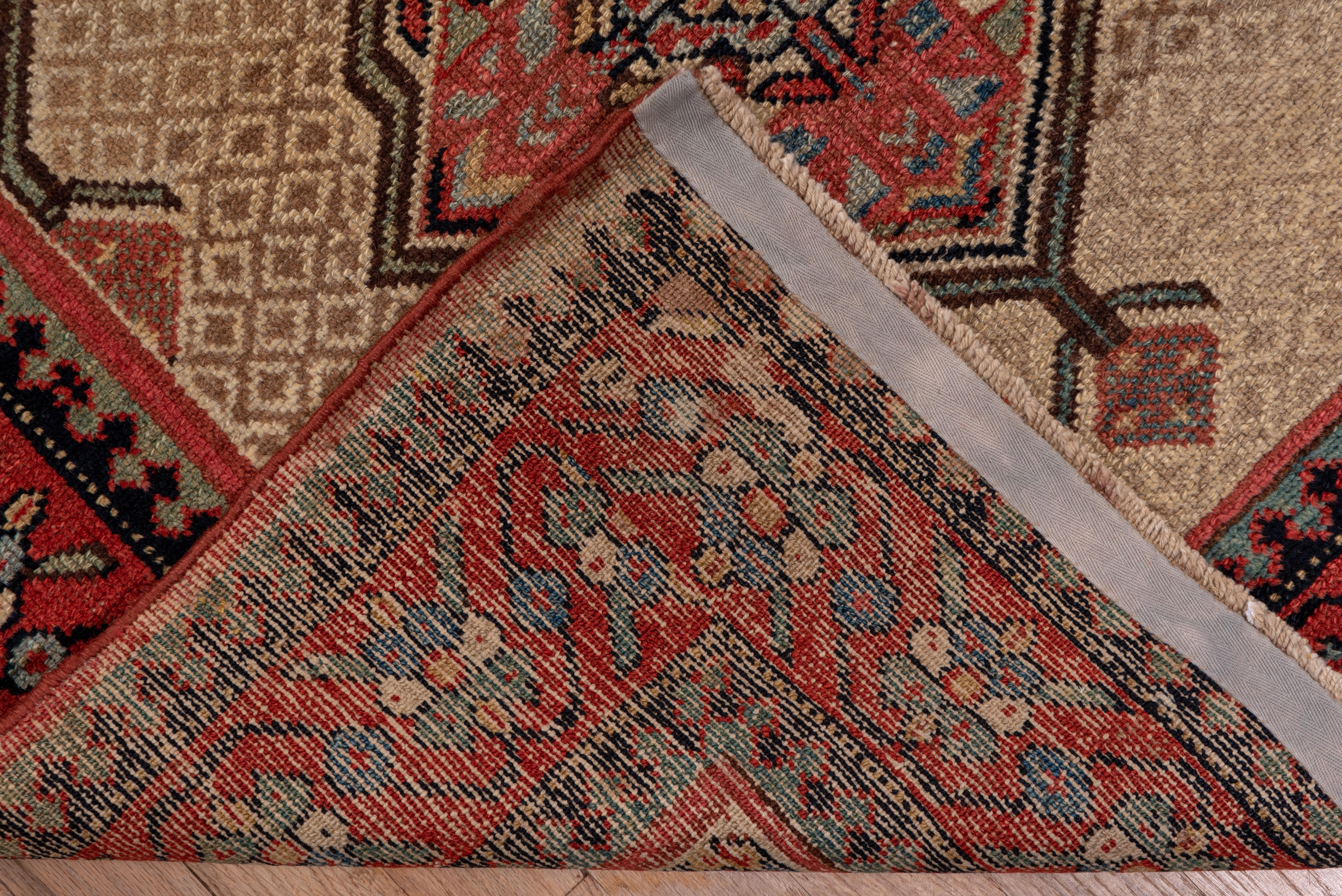 Seven geometric, pointed medallions with four radiating palmettes around cross centers, float easily on the two tone camel field with fractional fillers at sides and corners. Red border with reversing winged palmettes. Medium rustic weave on cotton.