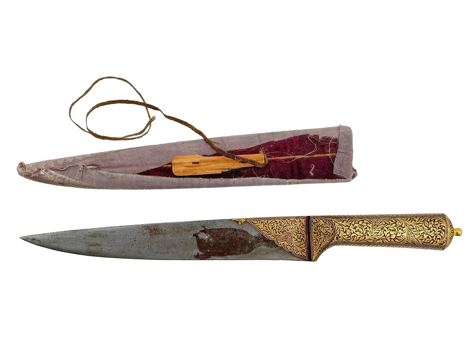 An antique Persian damask steel Kard knife with a scabbard. The blade is made of damask steel, flat, single edged, without fullers, the combat end is double edged. The handle and part of the blade are richly decorated with gold tone foliate