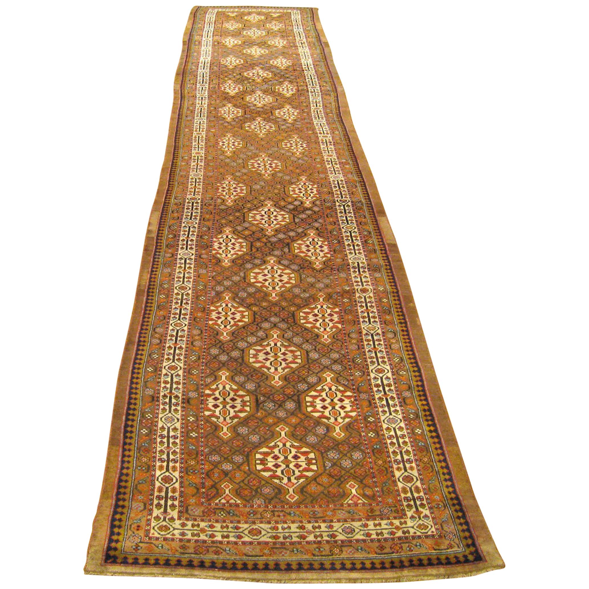 An antique Persian Hamadan Camel Hair oriental rug, in long runner size, with a repeat design in the central field.  Circa 1900.  Size 21'9 x 3'9.  This antique hand-knotted wool runner features an allover lozenge design surrounded by repeating
