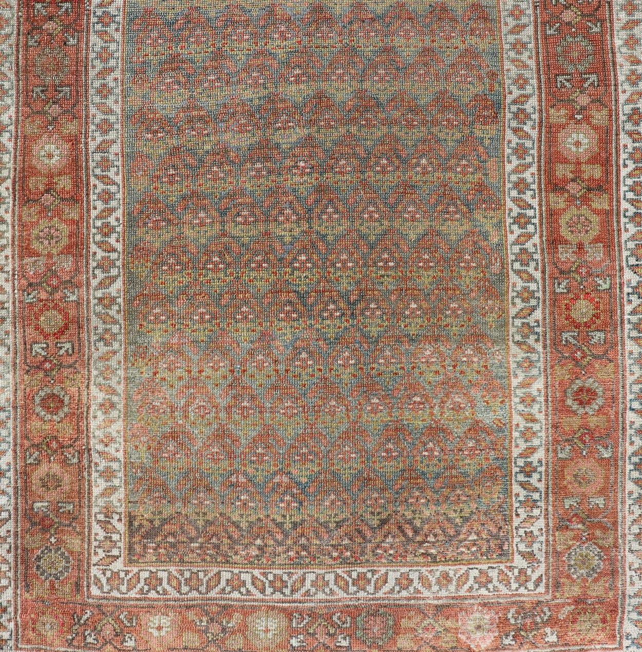 This antique Persian Hamadan rug has been hand-knotted in wool and features an all-over sub-geometric design rendered in red's, pink, green, and shades of blue. A complementary, multi-tiered border encompasses the entirety of the piece; making it a