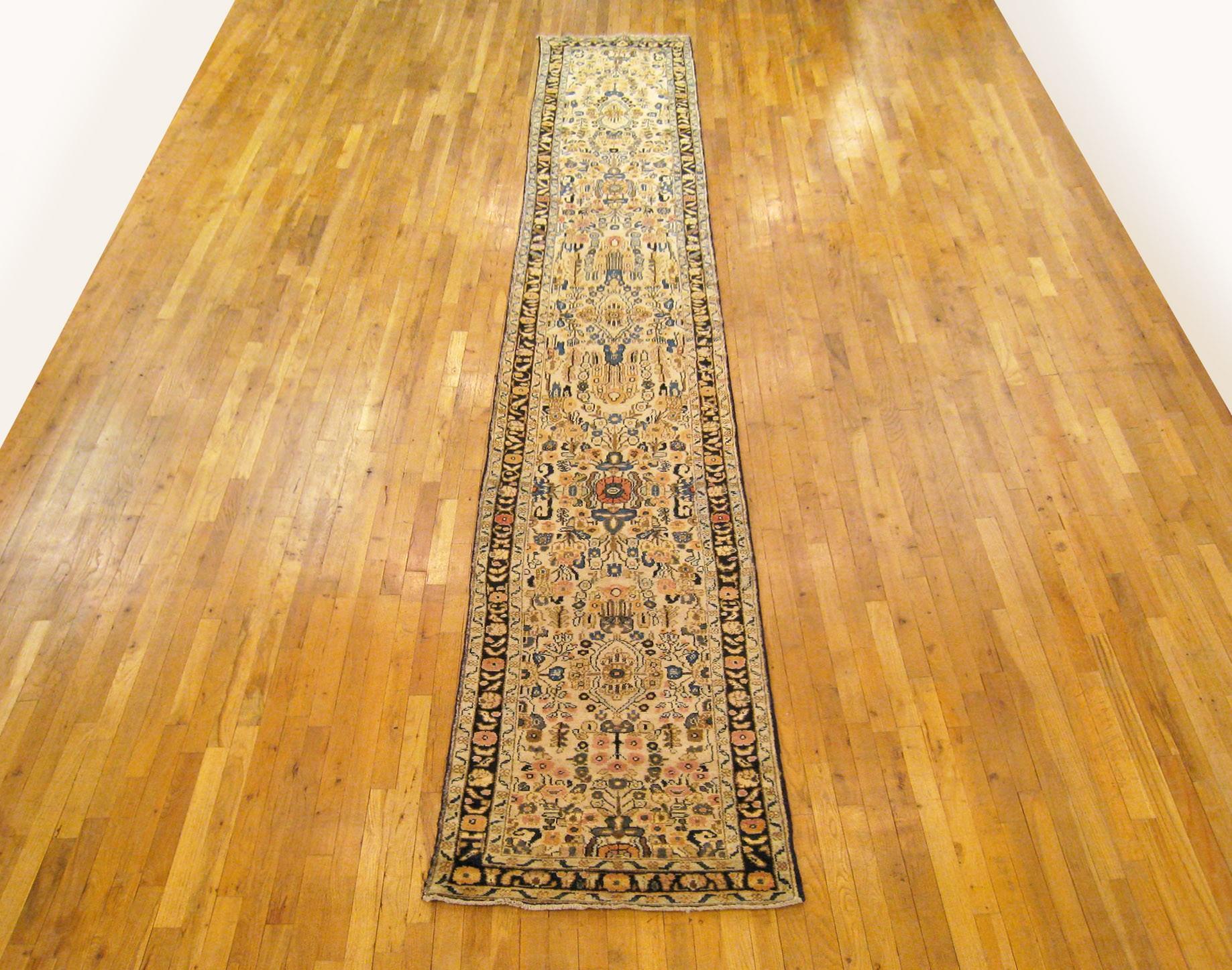 A vintage Persian Hamadan Oriental rug in runner size, size 16'6 x 2'6, circa 1930. This lovely hand knotted carpet features a dazzling floral design in the ivory central field, alternating between small scale and large scale floral elements. The