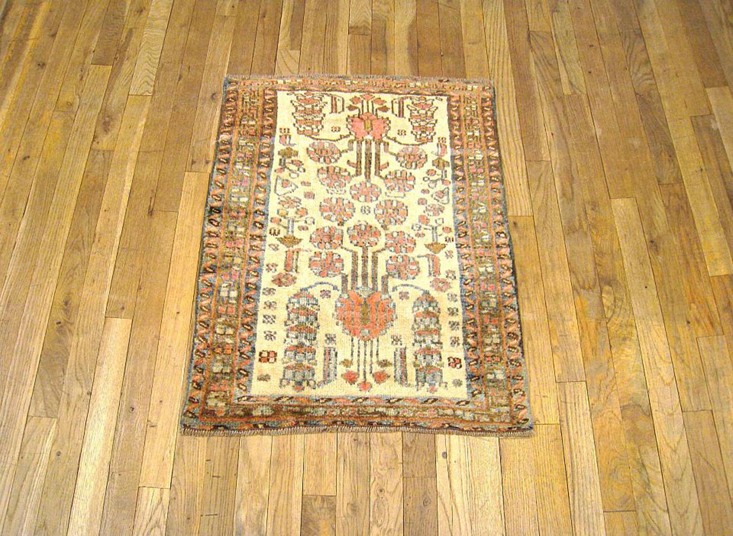 An antique Persian Hamadan oriental rug, size 2'9 H x 2'2 W, circa 1920. This lovely handwoven rug features an ivory central field, which is rare for this type of rug in this size, and a stylized design of flower heads and floral sprays. The central