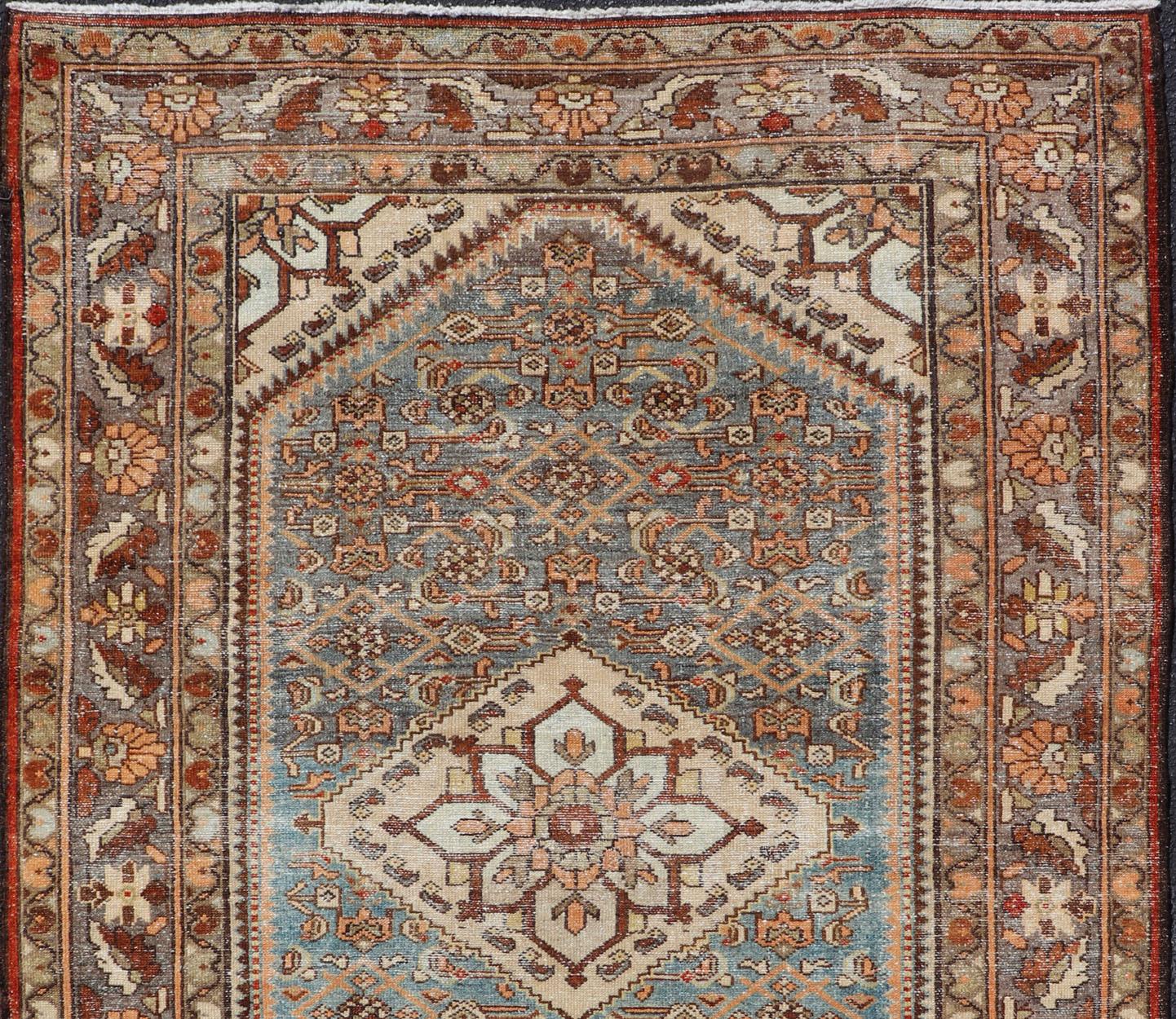 This antique Persian Hamadan rug features a layered medallion with sub-geometric flowers design, and is enclosed within a complementary, multi-tiered border. Rendered in blue and earthy tones; this rug is a good fit for a variety of classic,