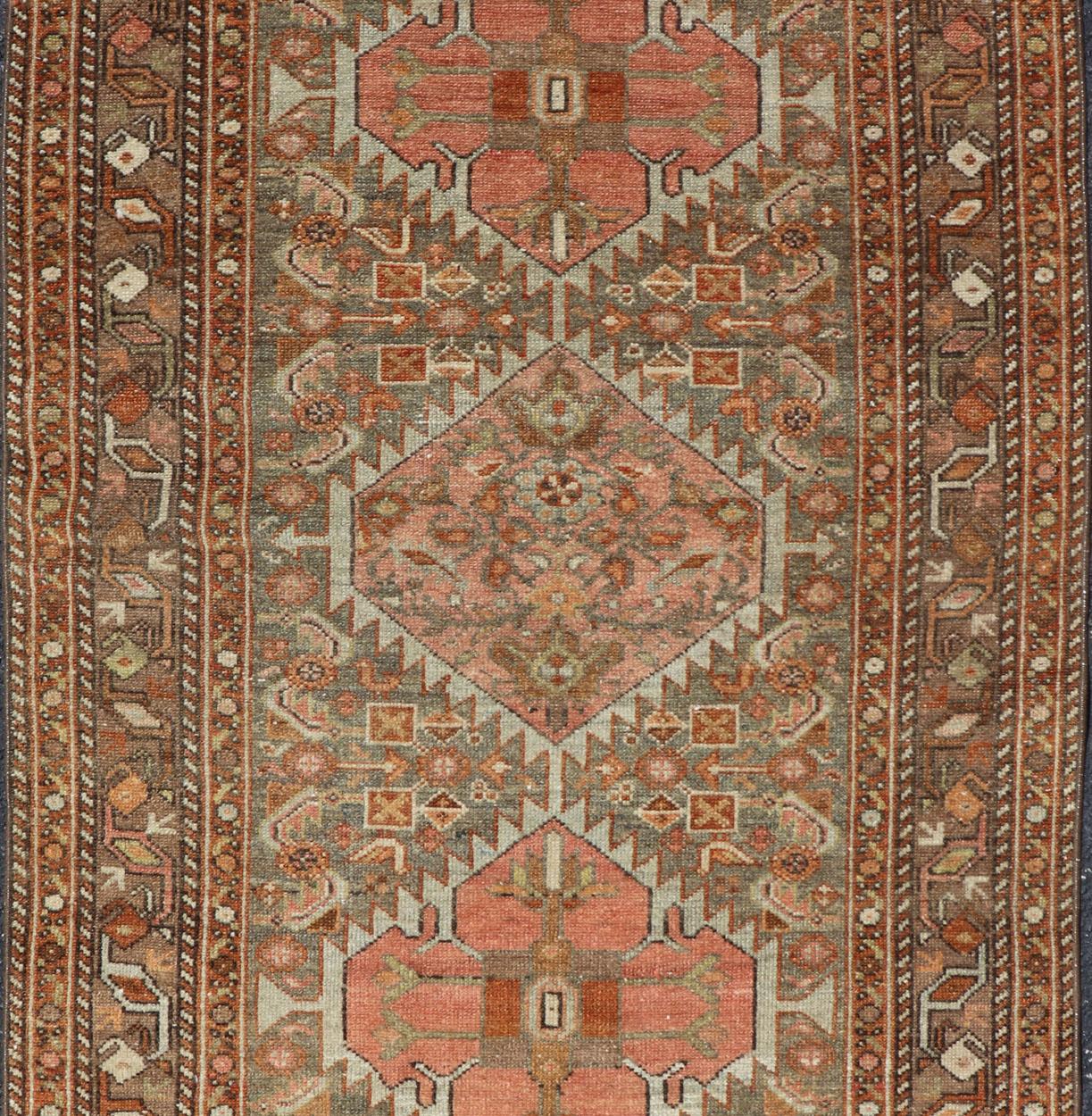 This antique hamadan features three medallions in the field, surrounded by sub-geometric tribal motifs. The complementary border displays a geometric tribal design, wrapping around the entirety of the rug. Rendered in rusty reds, bronze, terracotta,