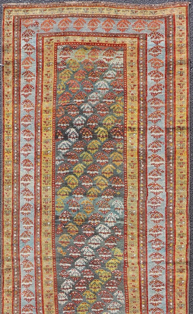 Dieser antike kurdische Läufer aus Persien ist aus Wolle handgeknüpft und zeigt ein mehrfarbiges subgeometrisches Muster, das sich über die gesamte Fläche erstreckt. Eine komplementäre, mehrstufige Bordüre umgibt das gesamte Stück und macht es zu