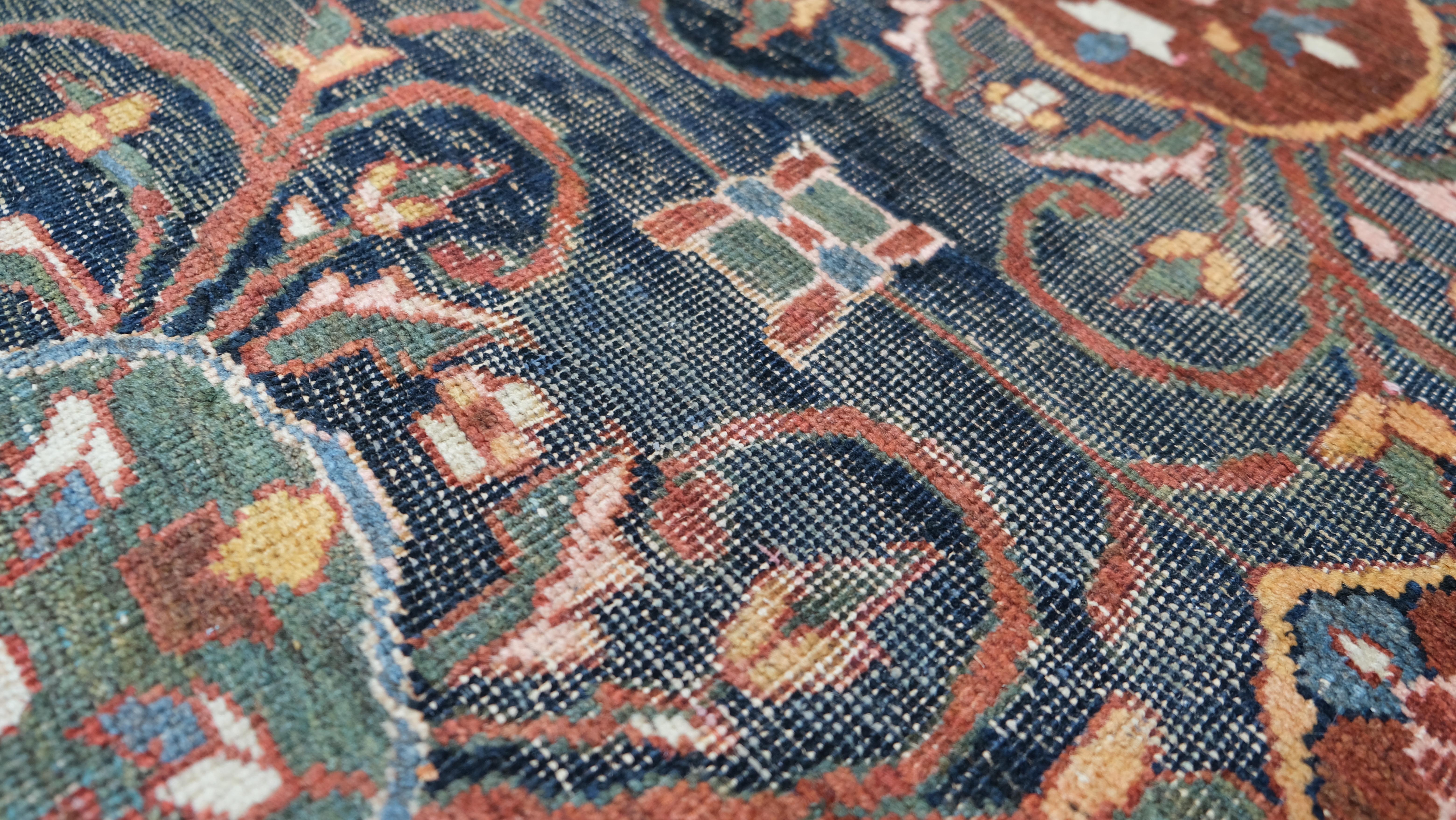 Ce tapis persan noué à la main, mesurant 5,3 x 9,10 pieds, présente un motif Herati sophistiqué à l'intérieur d'un médaillon saisissant. Le champ bleu nuit profond est orné de motifs floraux et de vignes interconnectés, créant un rythme visuel