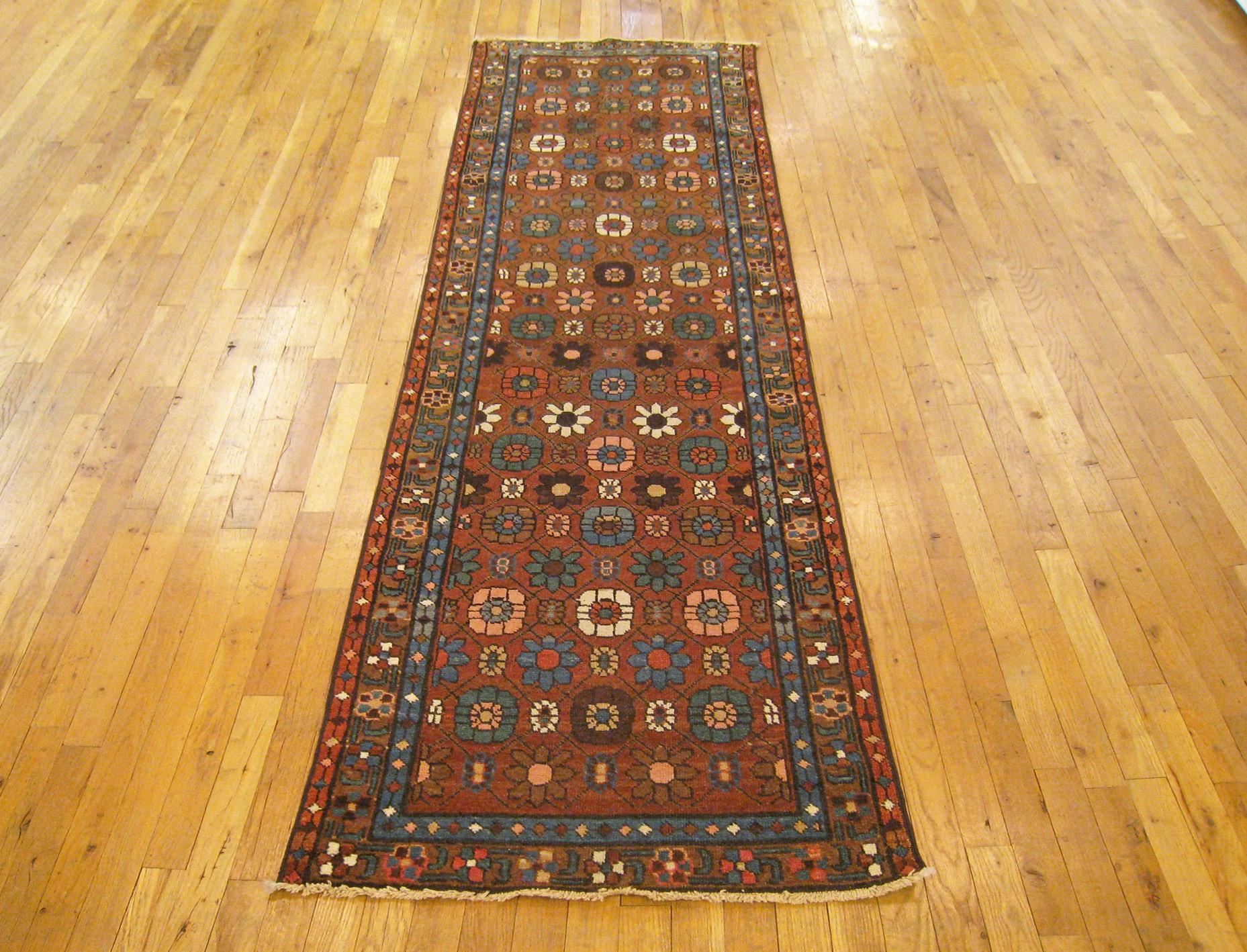 An antique Persian Heriz oriental rug in runner size, size 9'0 x 2'6, circa 1920. This handsome hand-knotted carpet features a stylish all-over flower-head design in the dark red central field. The field is enclosed within a well crafted dark red