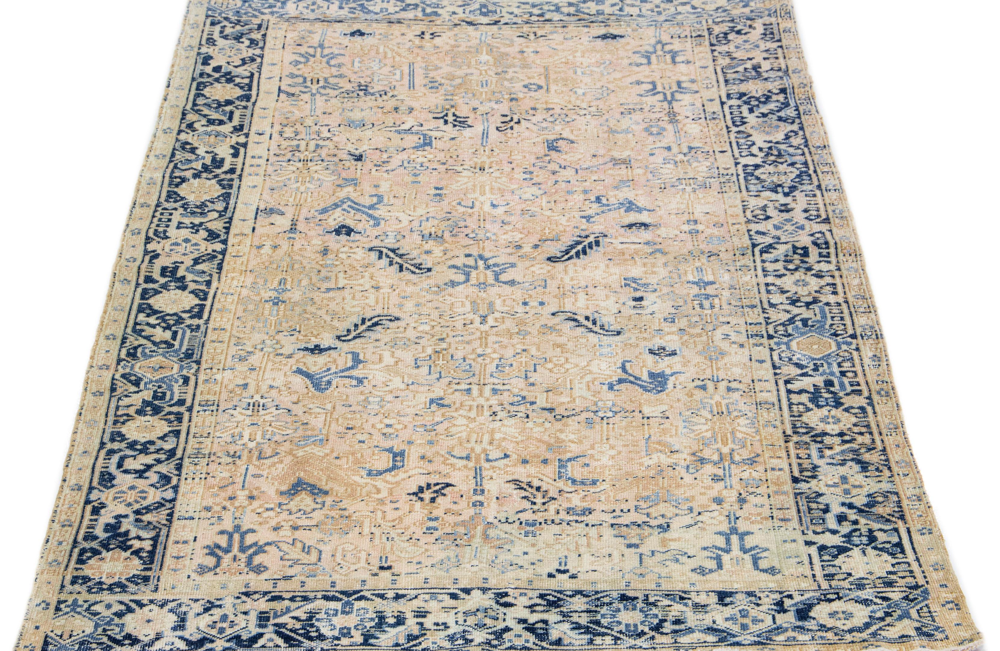 The antique Heriz rug exudes timeless elegance and sophistication with its premium hand knotted wool and striking all-over design. The eye-catching geometric floral pattern in shades of blue and beige adds a touch of allure to the soft peach field,