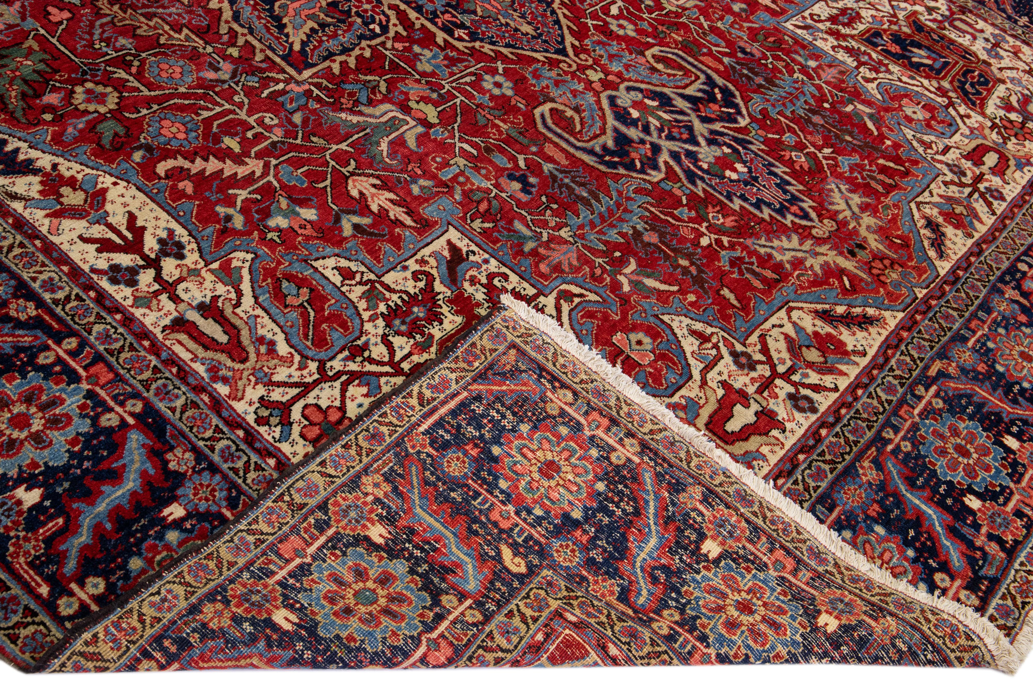 Beautiful Antique Heriz Serapi hand-knotted wool rug with a red field. This Persian rug has a navy blue frame with multi-color accents that feature a gorgeous all-over medallion design.

This rug measures: 11'4