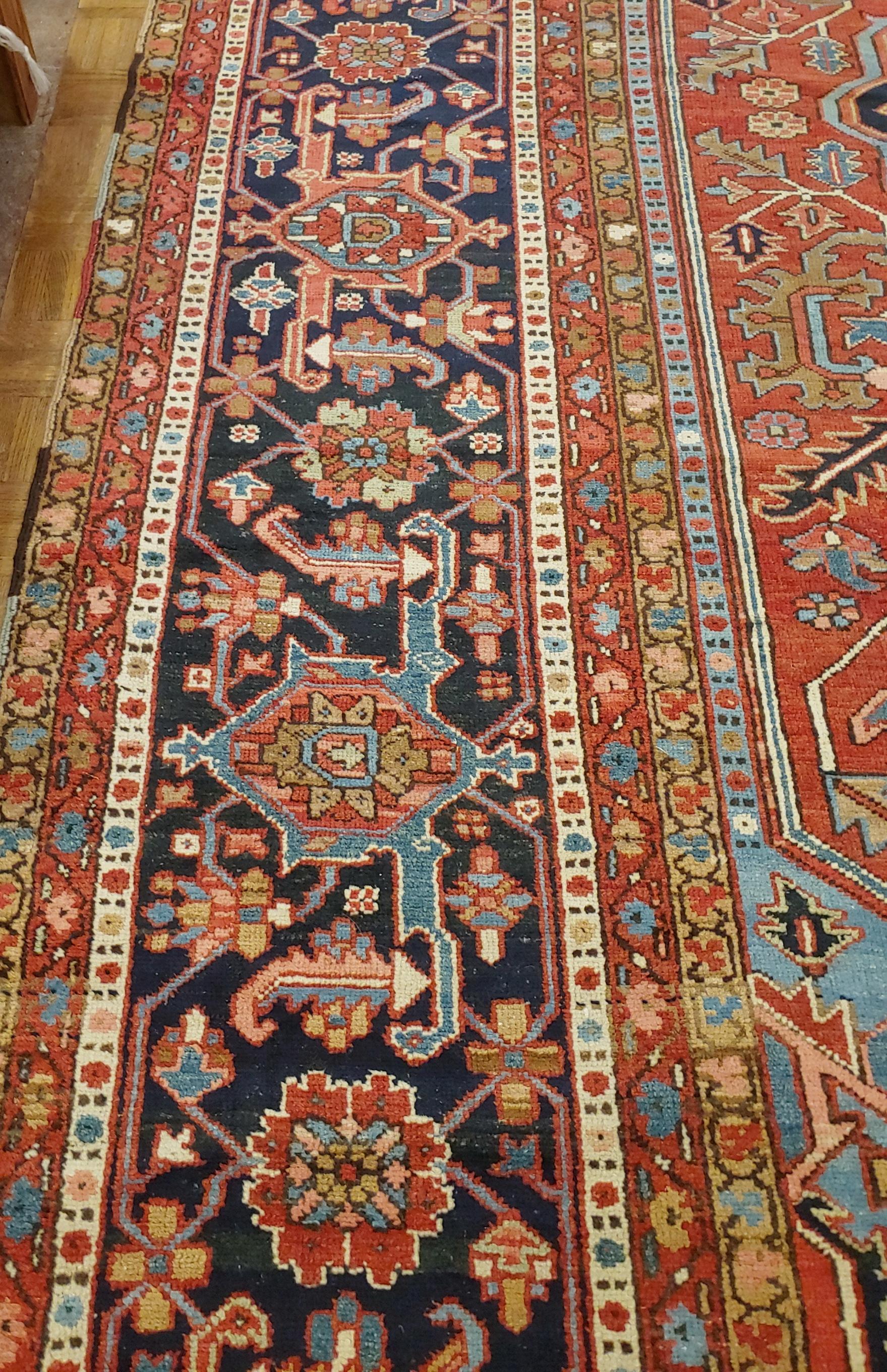 This palace size antique Persian Heriz rug from 1910 is 12-6 x 17-6. It is a Classic Heriz motif with a navy medallion and border on a red/rust field with highly decorative light blue corners.