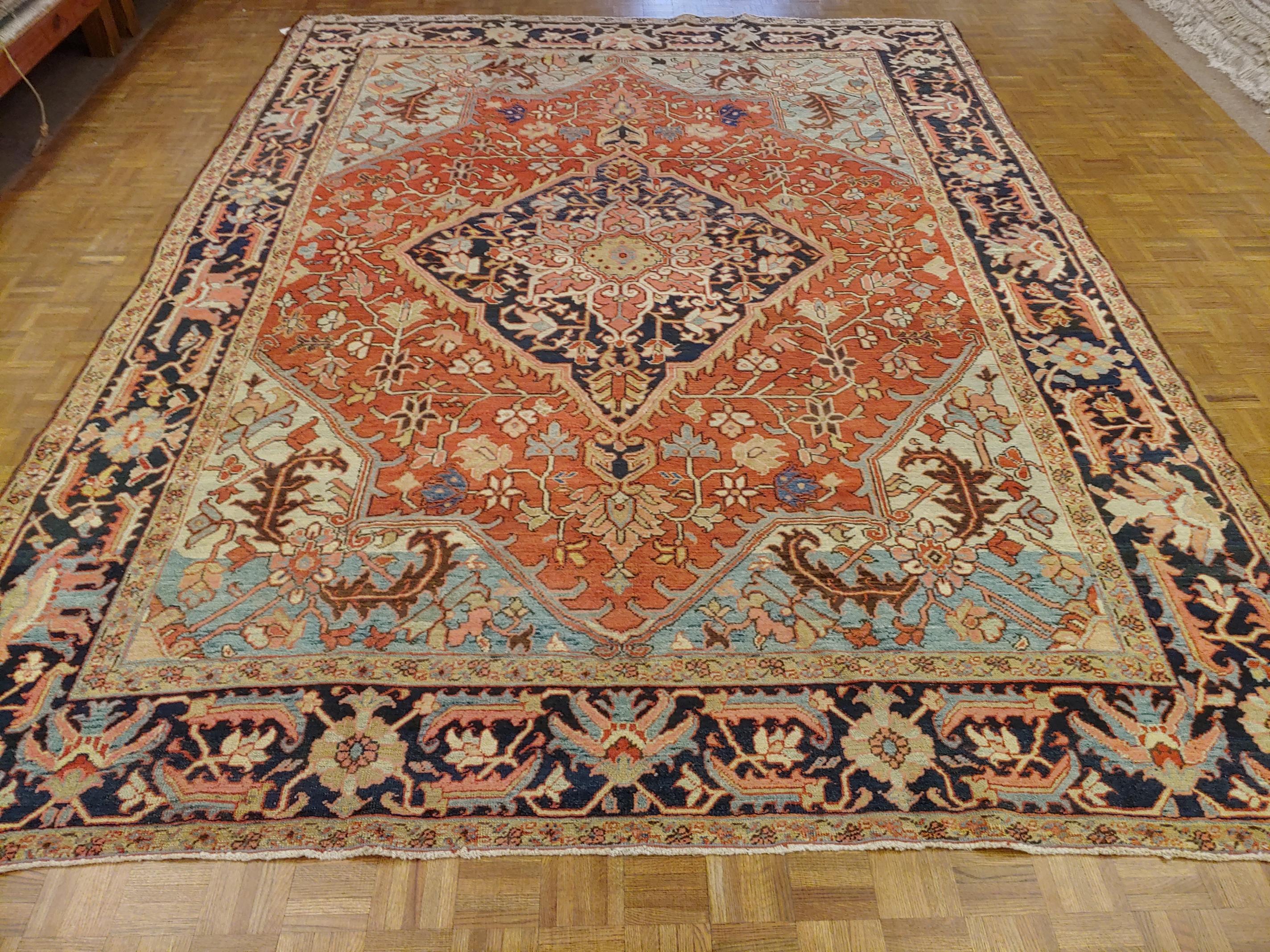 A magnificent antique Persian Heriz rug similar to a Serapi but not quite as old. It is a room size, about 9x12. This rug has a rust field with light blue corners and a navy border. The rug also uses a beautiful aubergine color as well. It also has