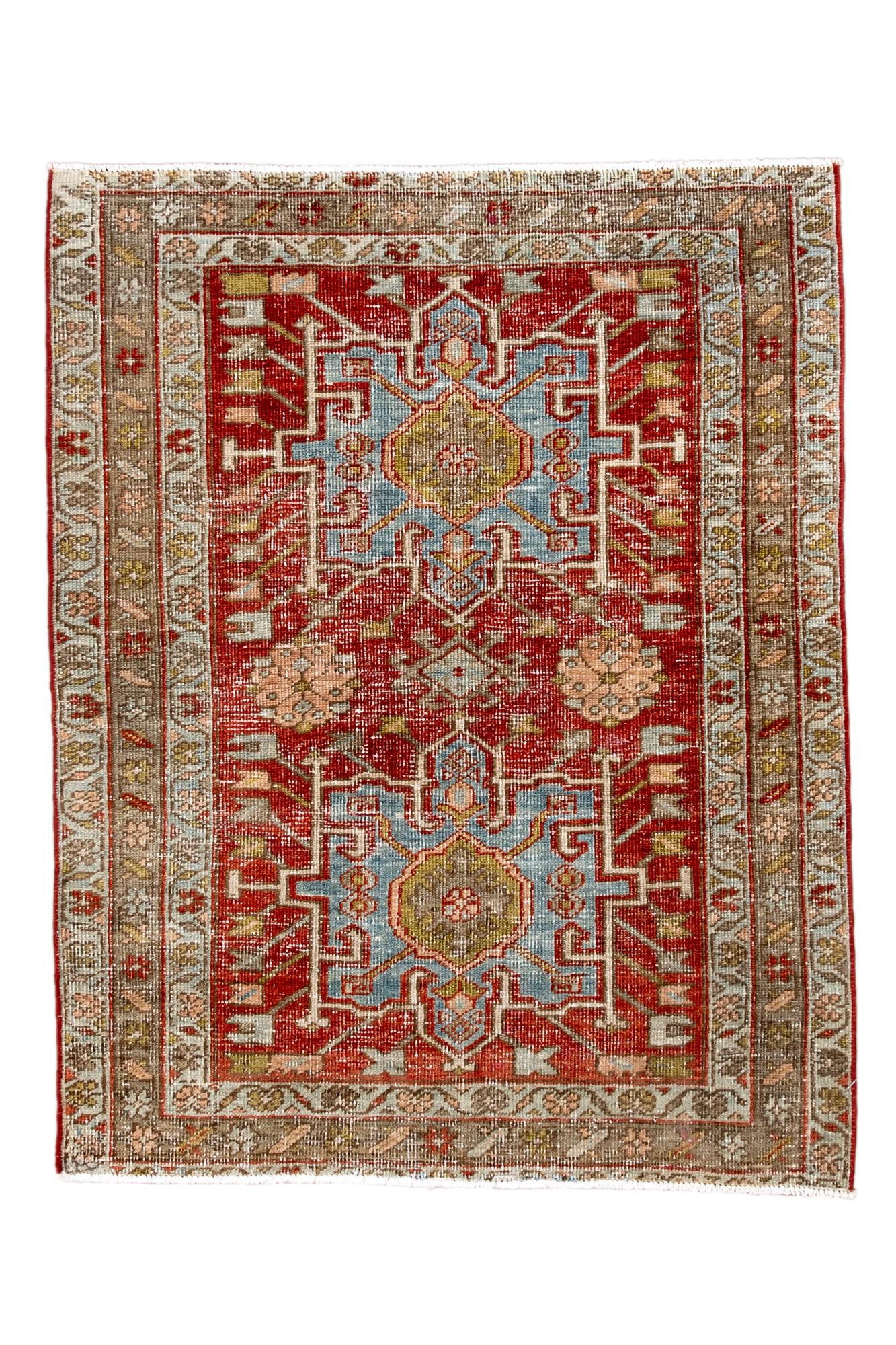 This small antique Heriz rug features two stacked geometric medallions in soft sky blue set against a brick-red field, surrounded by angular vine motifs and a camel-toned border. Despite its worn pile, the drawing remains clear, giving the piece a