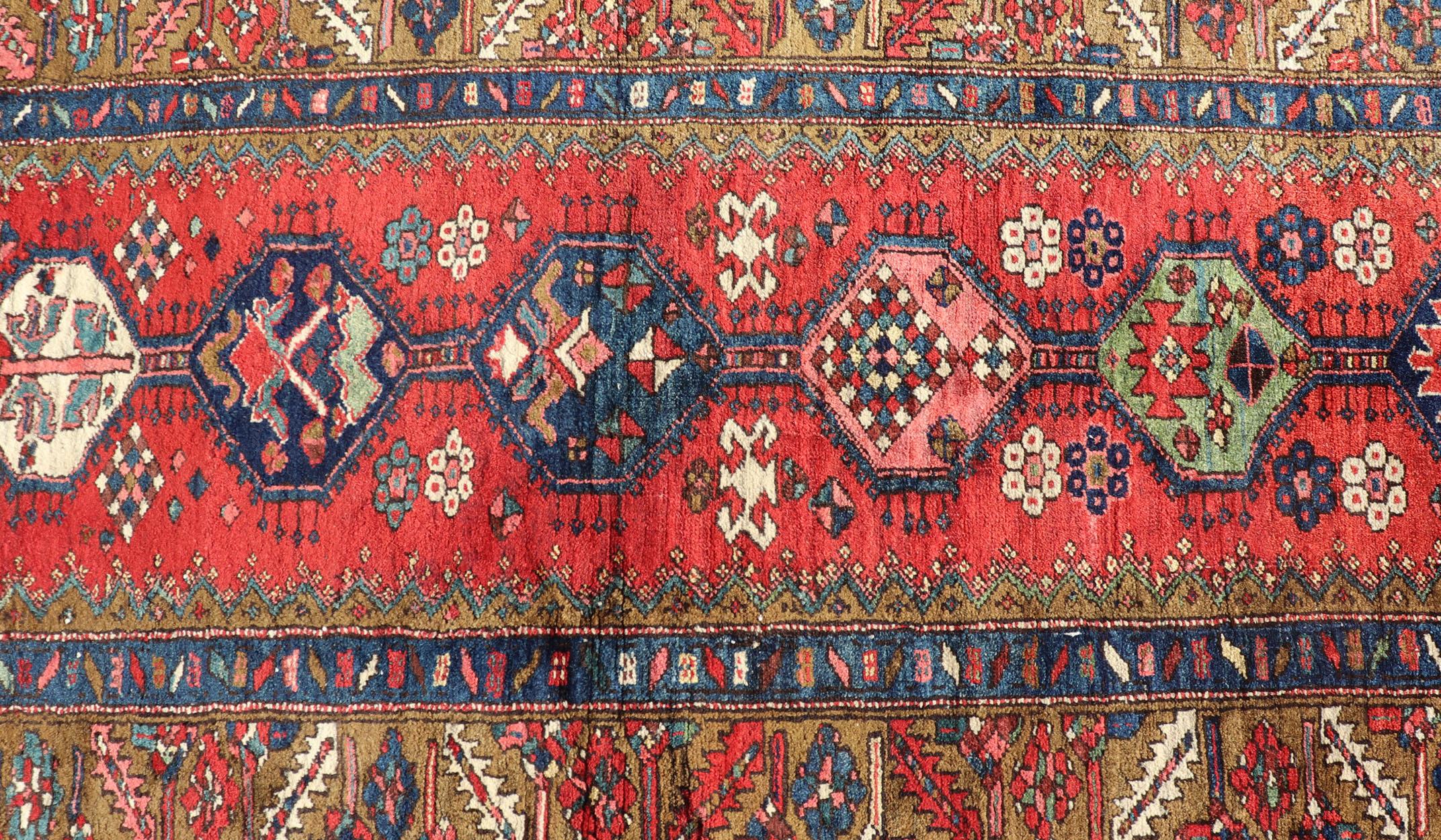This gorgeous antique Persian Heriz runner features a red background imbued with ornate medallions running along the piece. Sub-geometric designs decorate the field, and an intricate multi-tiered border surrounds the entirety of the piece. Colors