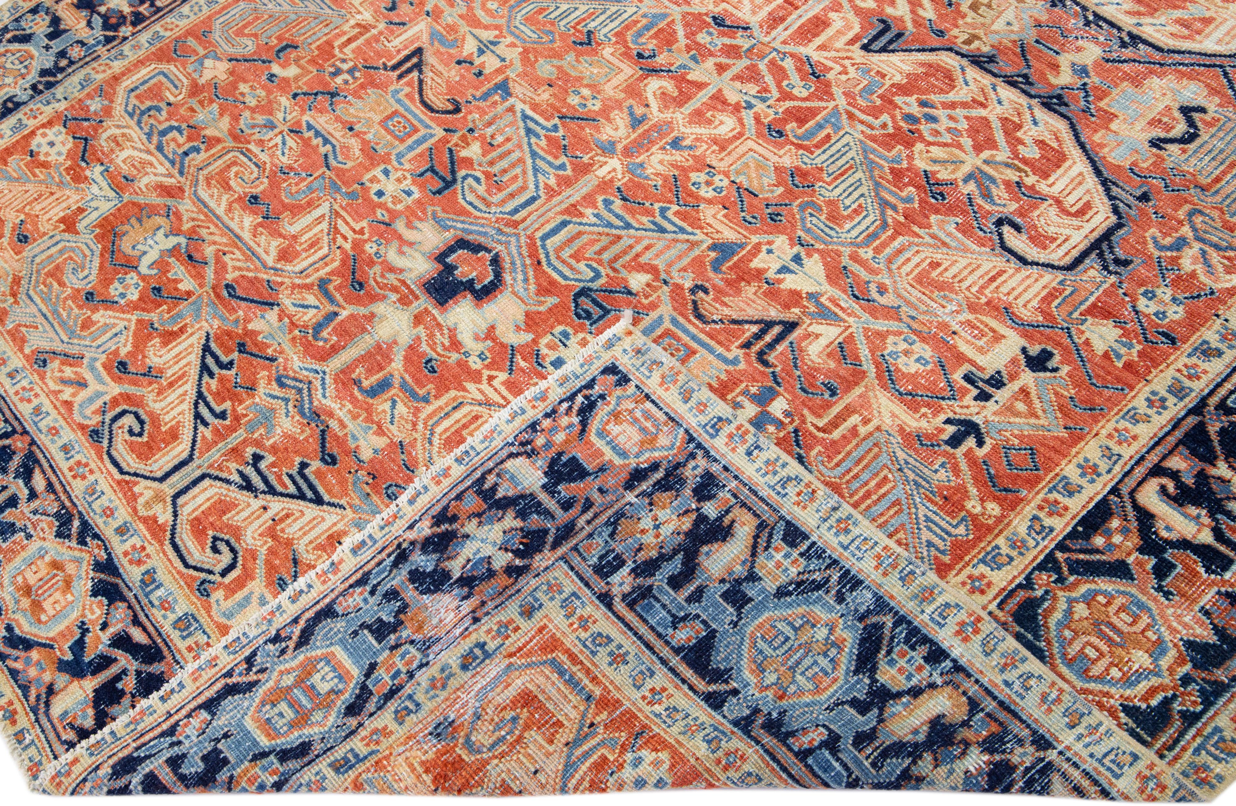 Beautiful antique Heriz hand-knotted wool rug with a rust color field. This Persian rug has a blue frame with beige and tan accents in a gorgeous all-over geometric medallion design.

This rug measures: 7'7