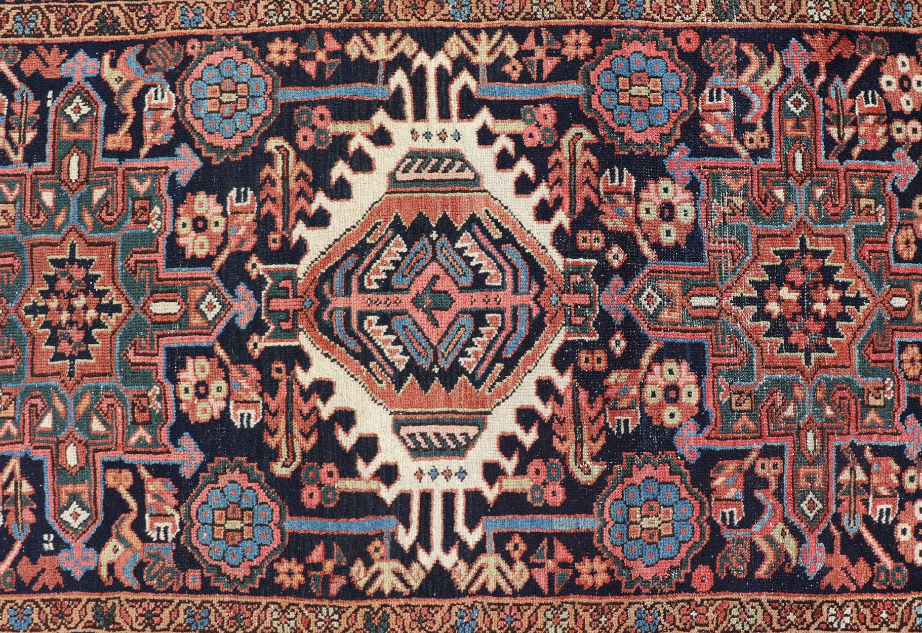This lovely Antique Heriz rug, hailing from northwestern Iran (circa 1920s), features a central medallion design surrounded by exquisitely defined geometric motifs. The rug has been rendered in Ivory, gorgeous hues of blue, orange and jewel tones.