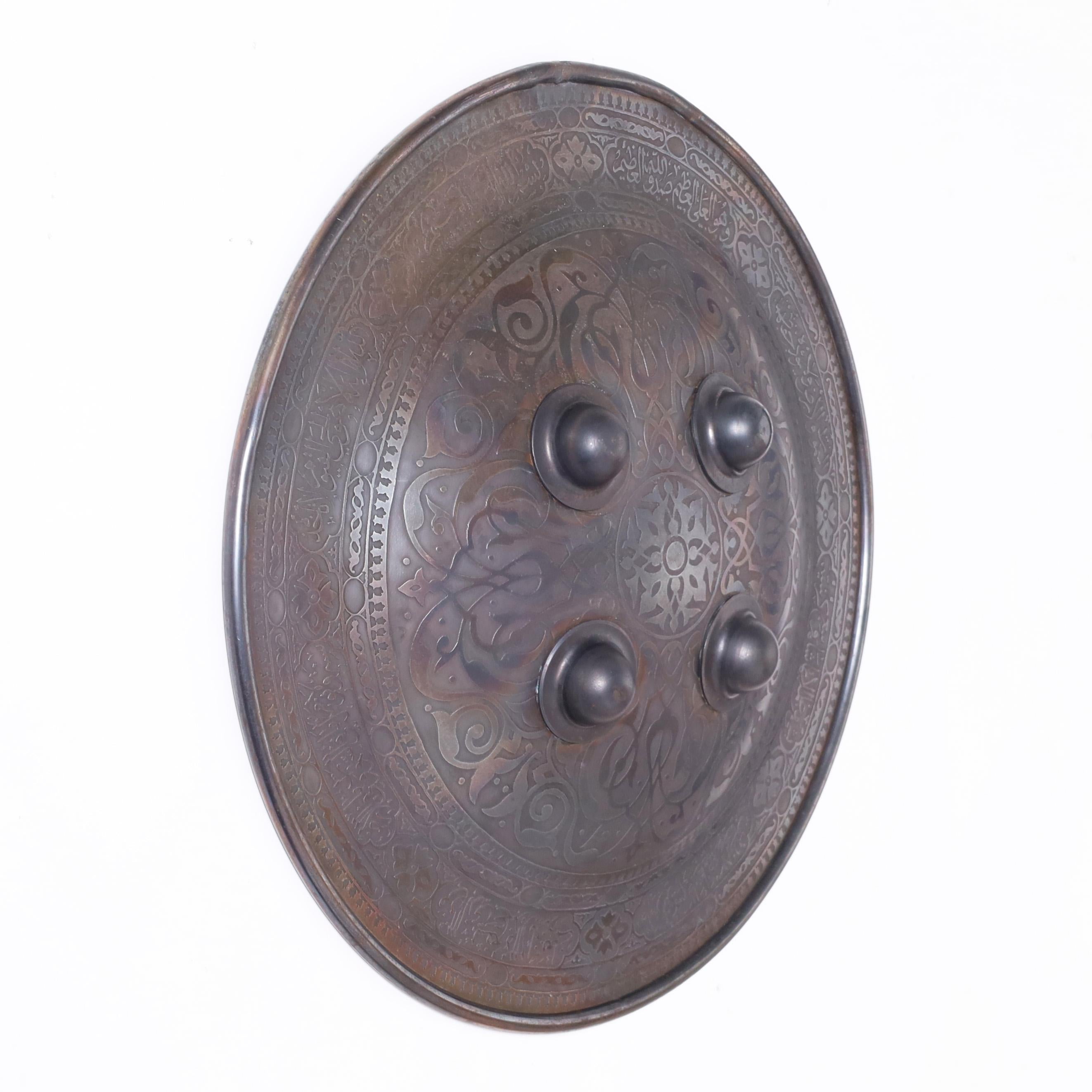 Transporting 19th century Persian Mughal shield crafted in iron and decorated in engraved floral designs and script.