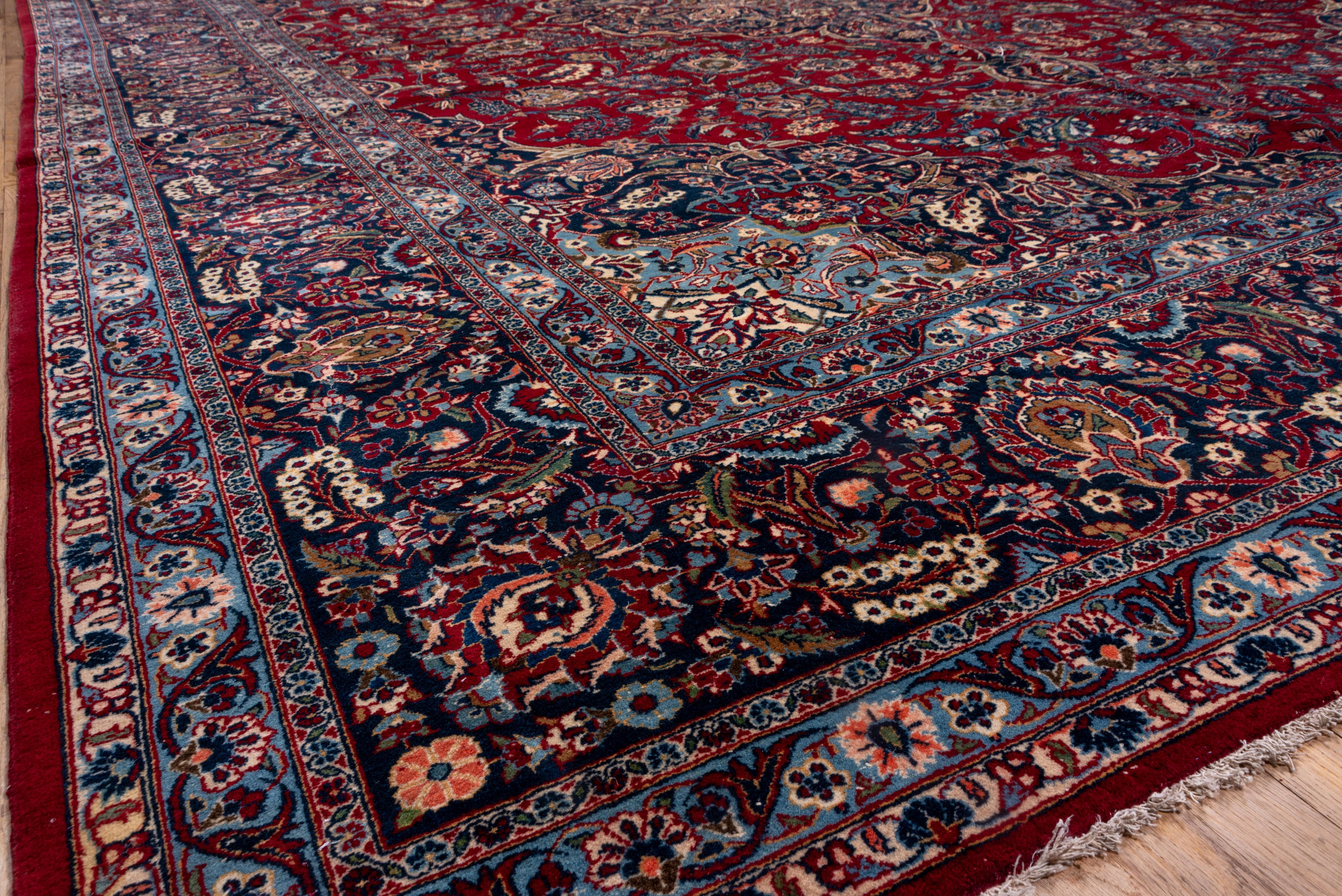 Classic red and navy central Persian town carpet with arabesque and acanthus-defined smaller medallion embedded in a complex array of palmettes, sickle leaves, and short racemes. Navy and cream corners. Royal/sapphire blue border with pointed oval