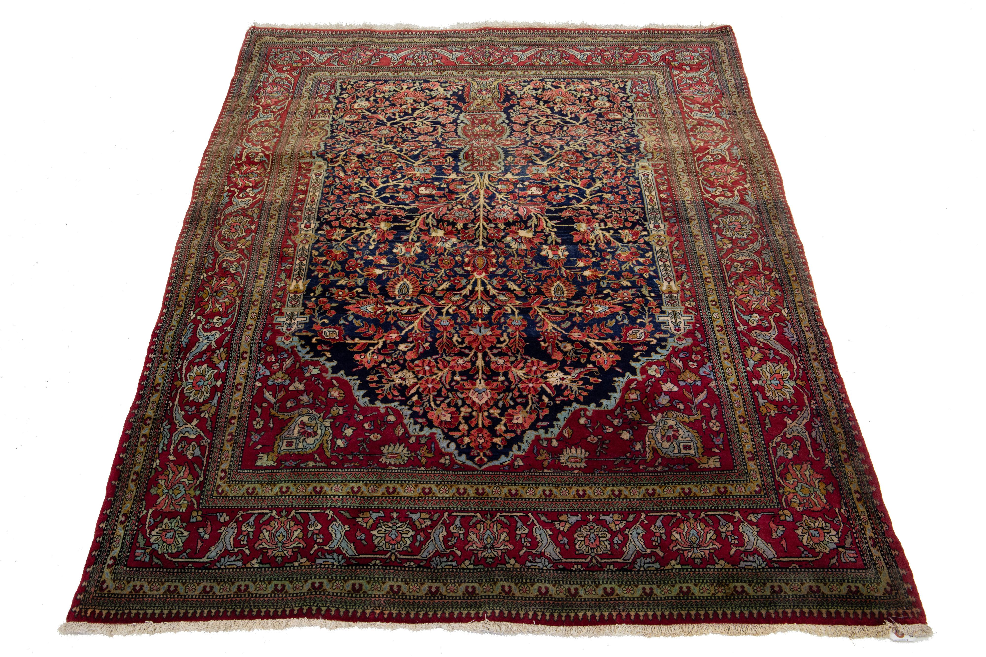 Magnifique tapis ancien en laine nouée à la main au Kashan, avec un champ bleu marine. Ce tapis persan a une bordure rouge et des accents multicolores, mettant en valeur un superbe motif floral en médaillon sur tout le pourtour.

Ce tapis mesure