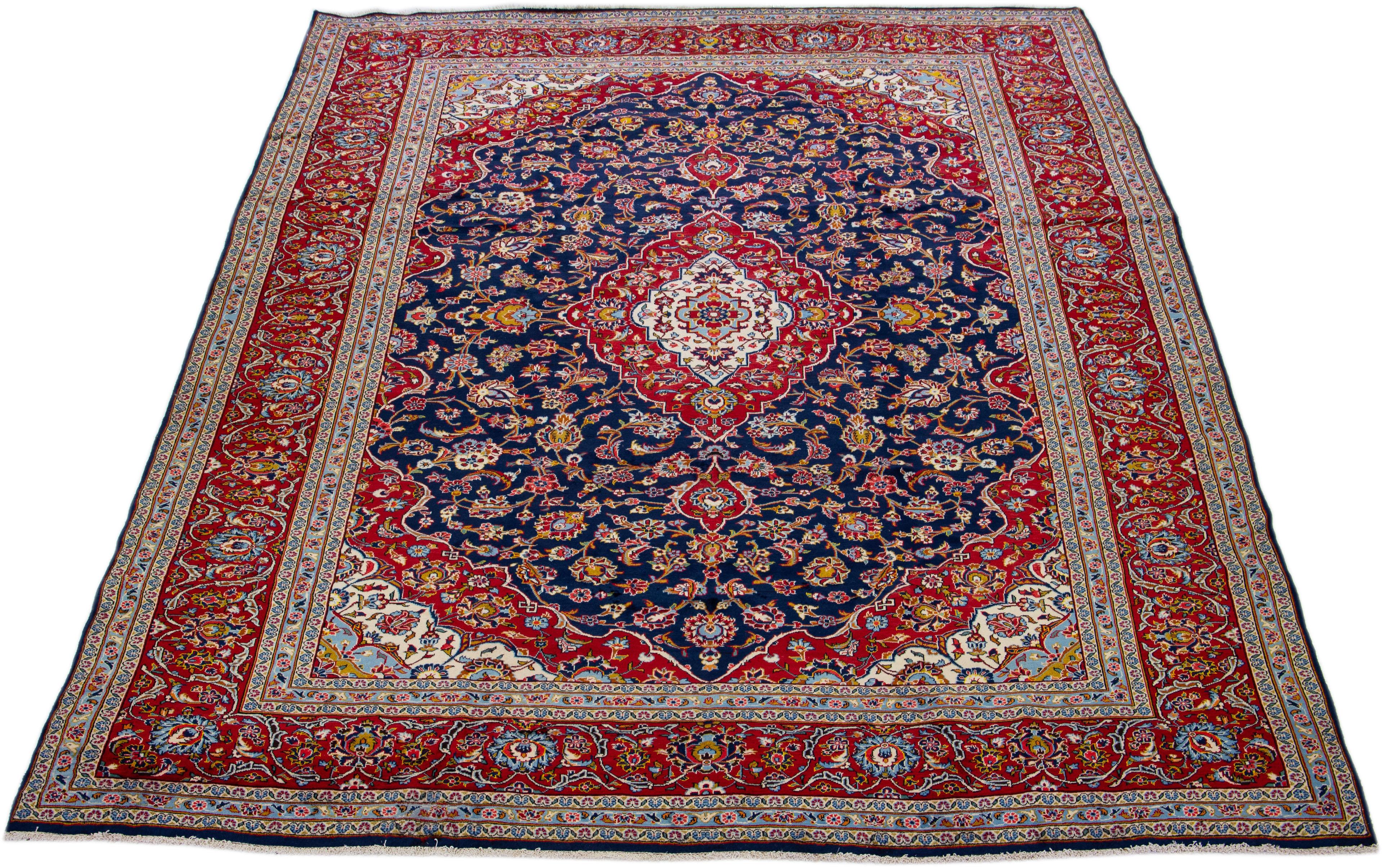 Beautiful antique Kashan hand-knotted wool rug with a navy blue color field. This Persian rug has a rusted frame and multicolor accents in a gorgeous all-over medallion floral design. 

This rug measures 10' x 13'3