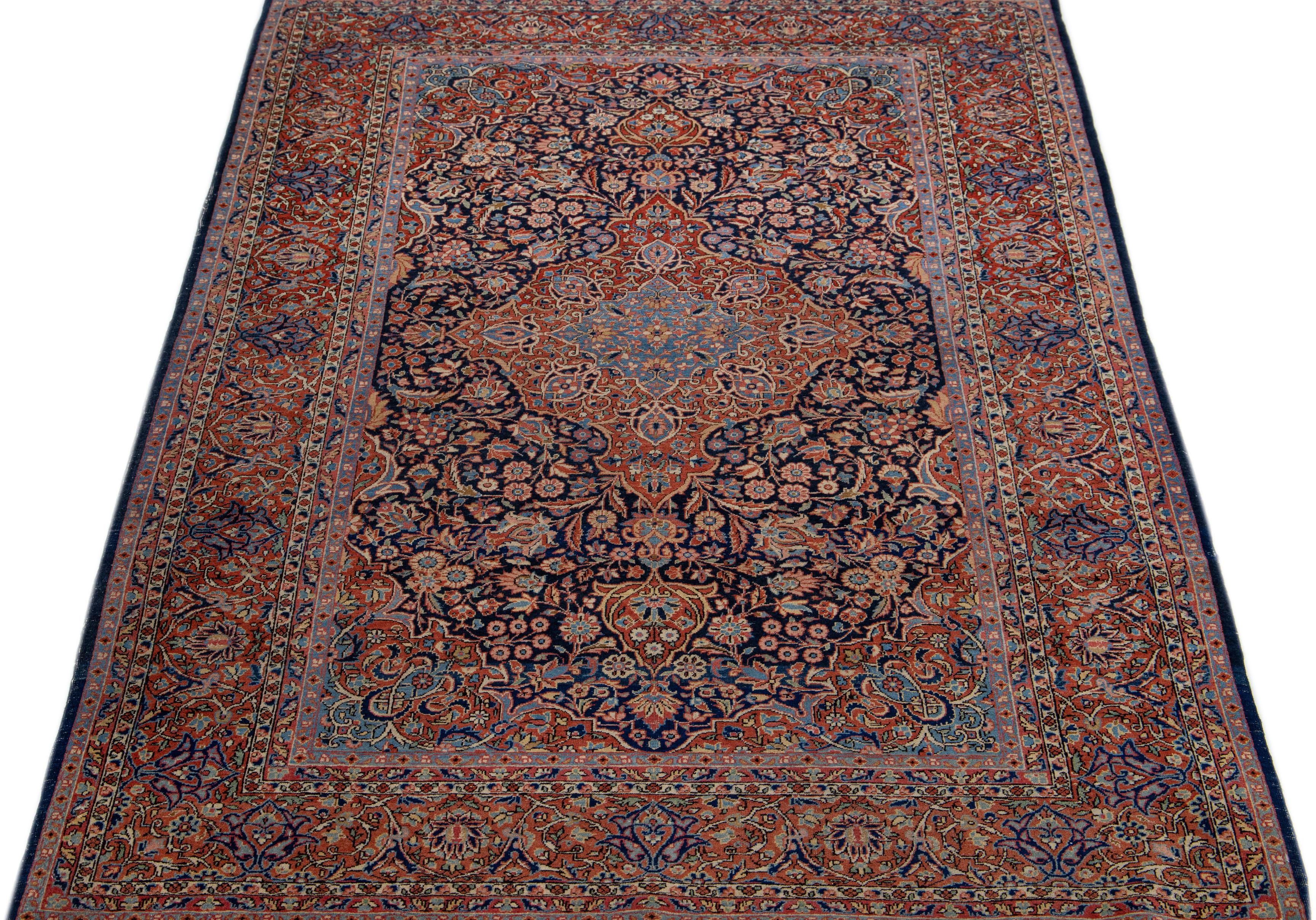 This antique Kashan hand-knotted wool rug boasts exquisite craftsmanship, featuring a finely woven navy blue field adorned with an all-over medallion floral design in red, pink, and beige accents. Magnificently crafted, this Persian rug is a