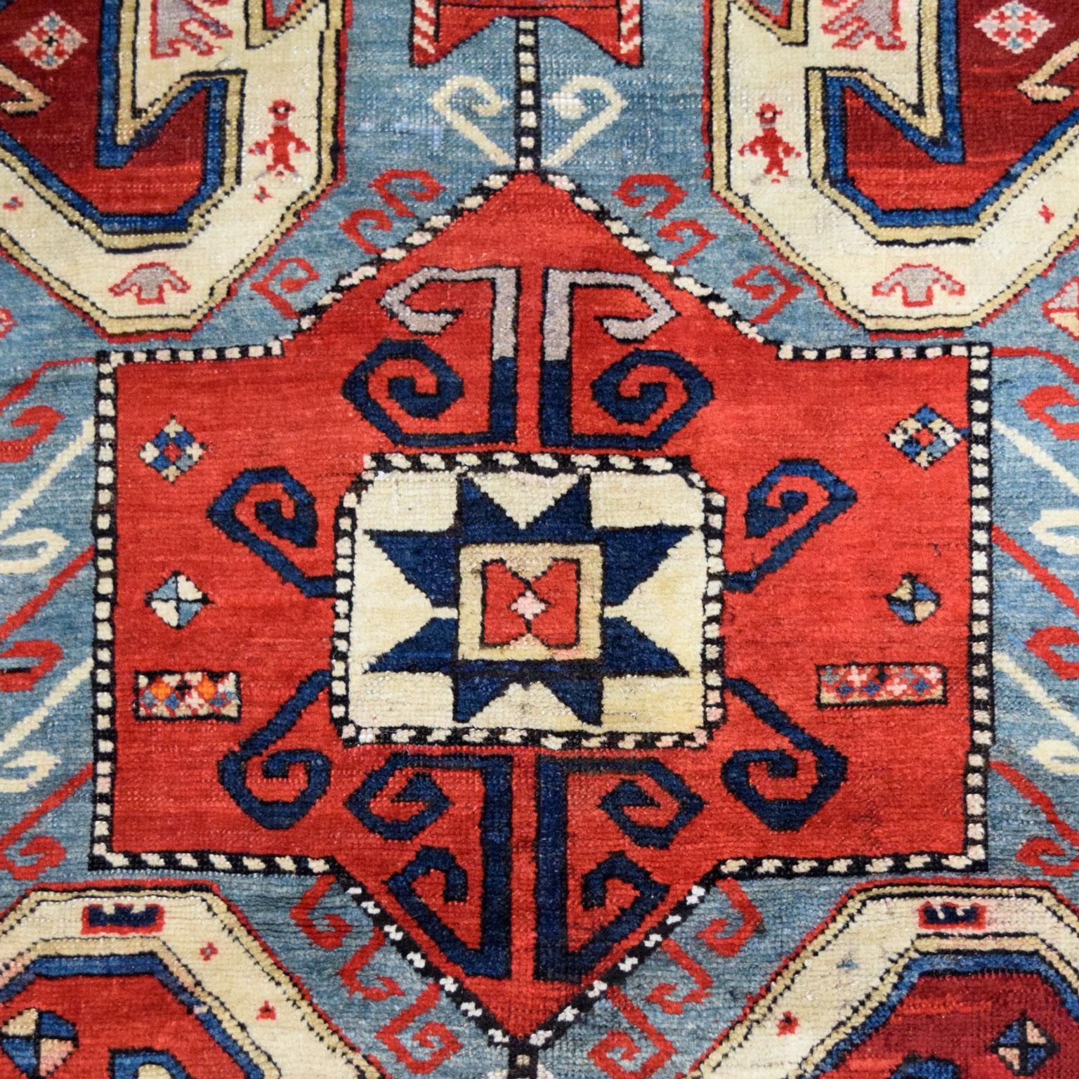 Hand-knotted in Iran, this blue, red, and cream Persian Kazak carpet measures 5’2” x 6’11” and belongs to Orley Shabahang’s Antique collection. Created using traditional Persian weaving techniques, this carpet features a luxuriously soft pile and a