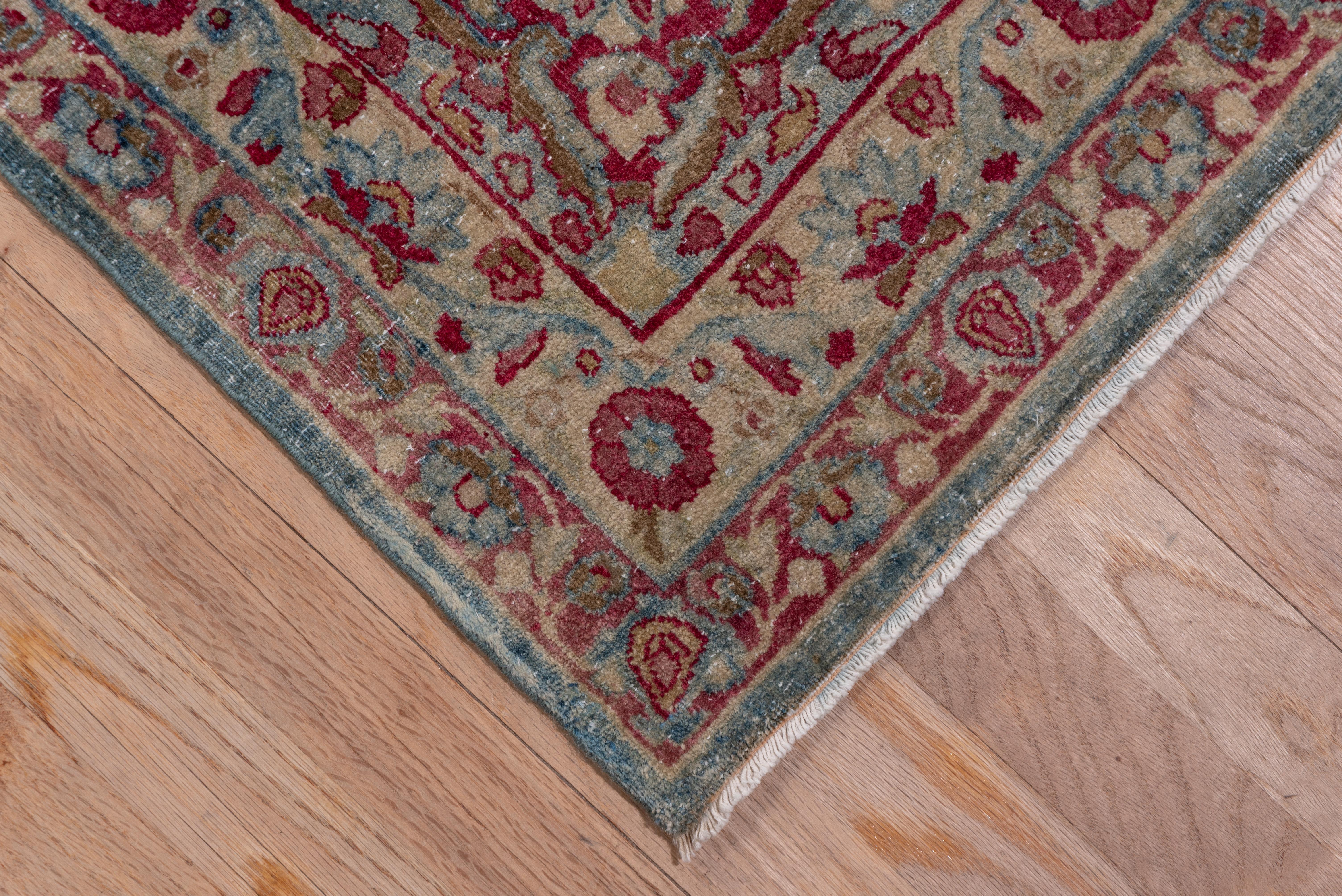 This predominantly light colored southeast Persian town carpet has a wine brown, pale green and ivory nested medallion with lozenge-shaped floral arrays. There are cypress trees in the pale green border as in the central medallion areas of wear,