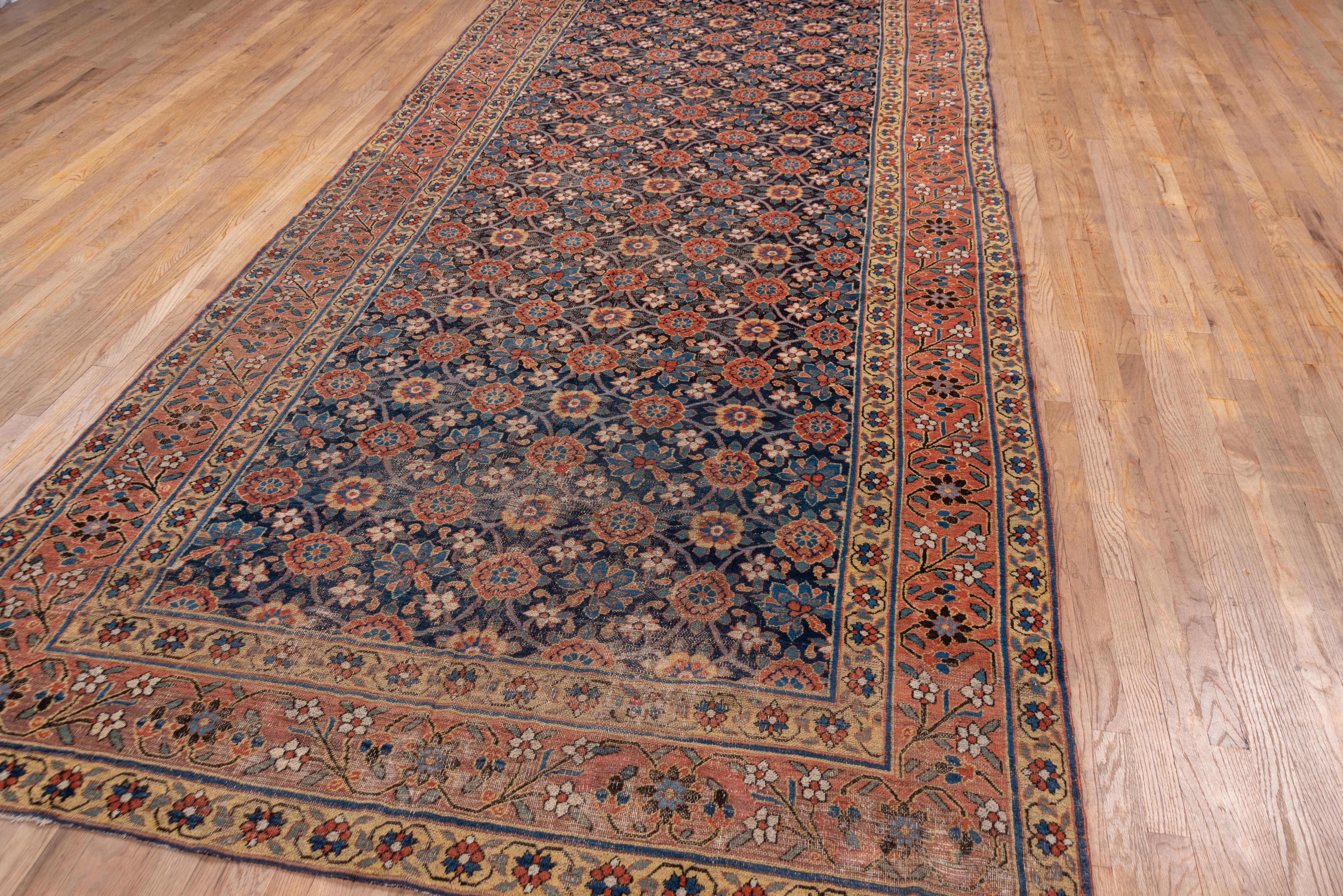 This clearly antique northeast Persian long carpet presents a royal blue ground supporting a rounded version of the popular all-over Mina Khani palmette trellis with contrasting off white prunus flowers and oblique stylized irises. The red border