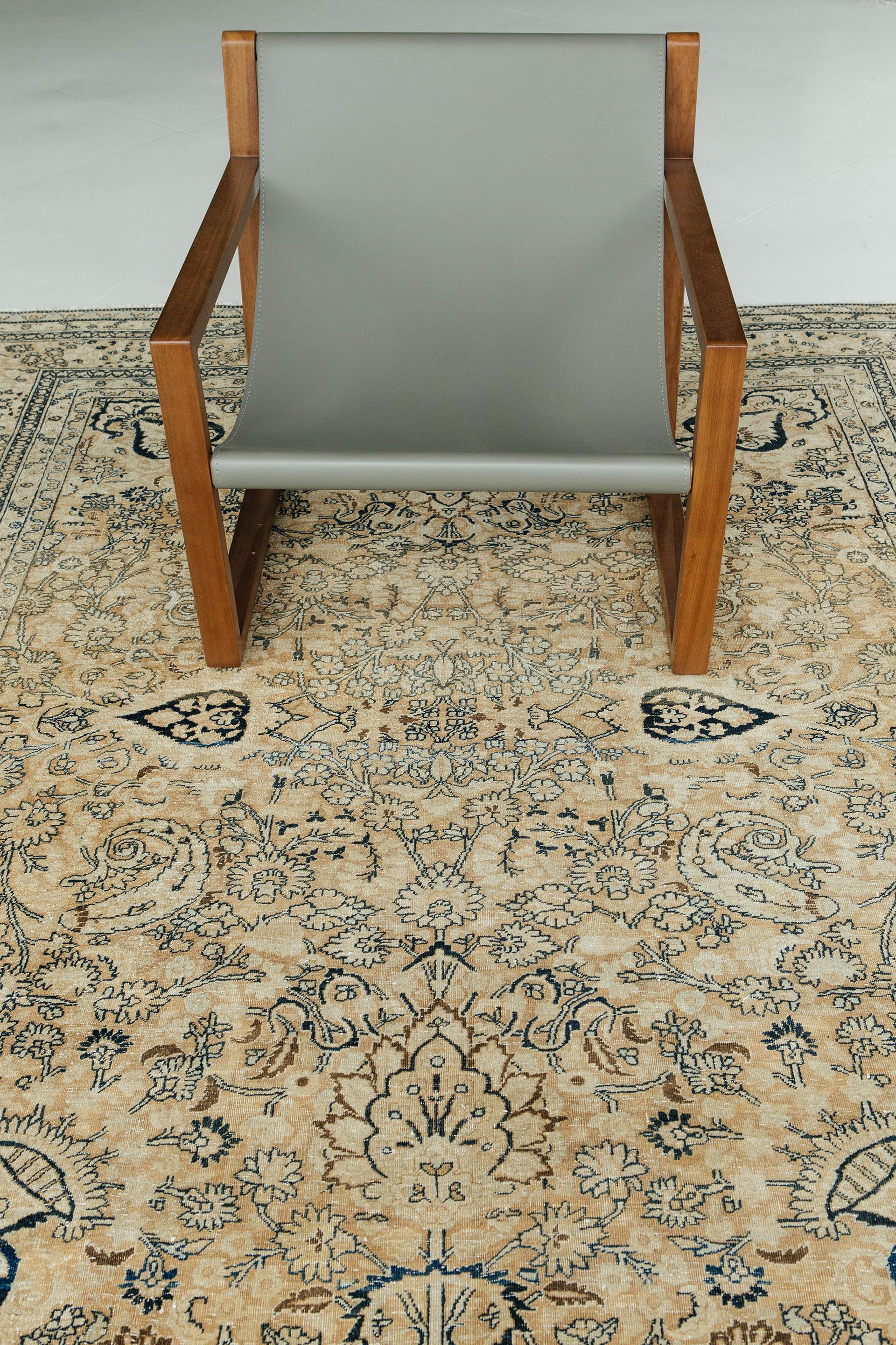 Soft brown ground with ivory and tan motifs delineated in deep indigo and dark brown colors. This rug brims with floral vines, palmettes, spiraling leaves and features vase motifs in each corner. The composition is framed by floral borders and