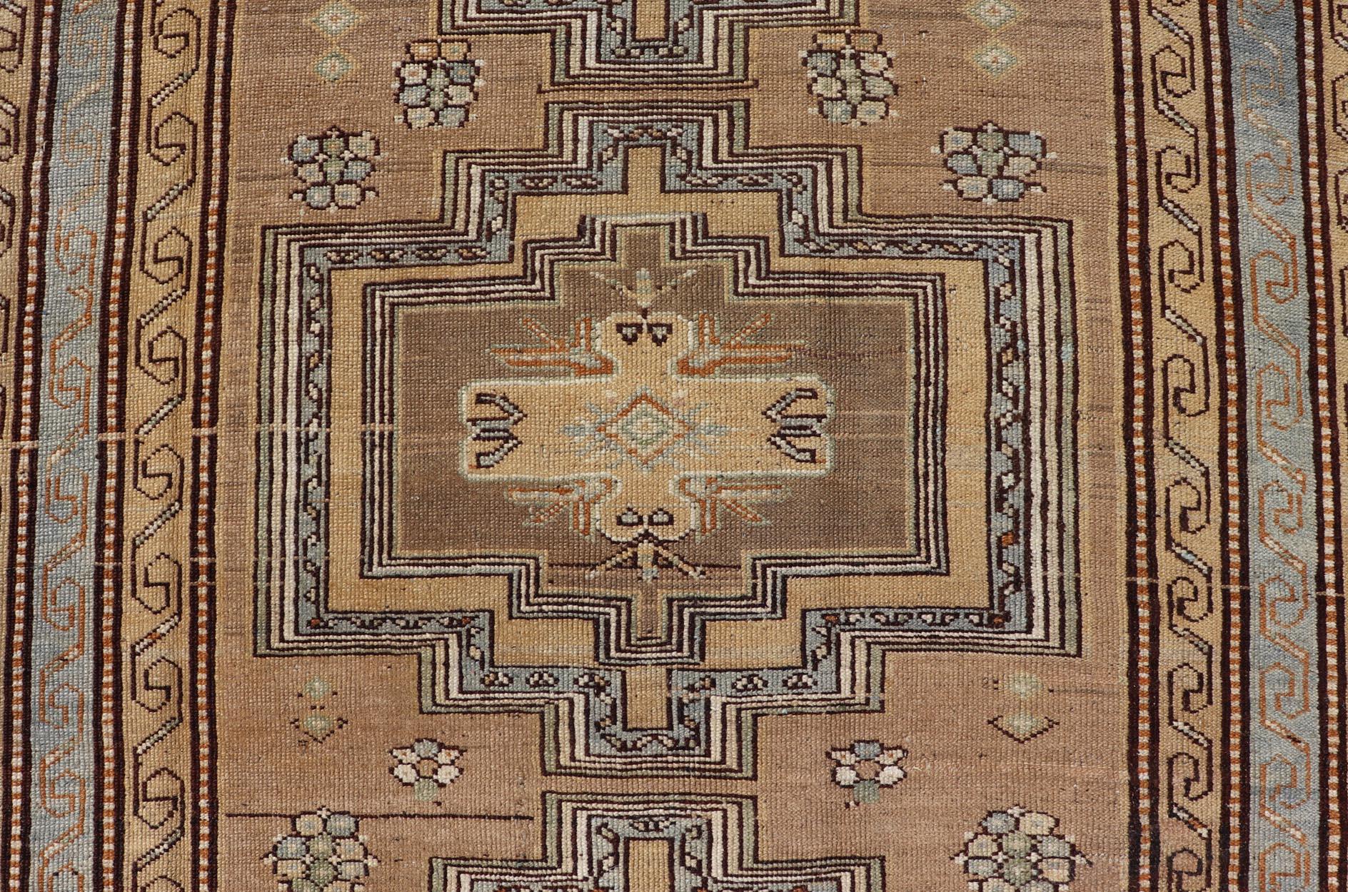 This antique Persian Kurdish rug has been hand-knotted in wool and features a large tri-medallion design rendered in blue-gray and earthy tones. A complementary, multi-tiered border encompasses the entirety of the piece; making it a marvelous fit
