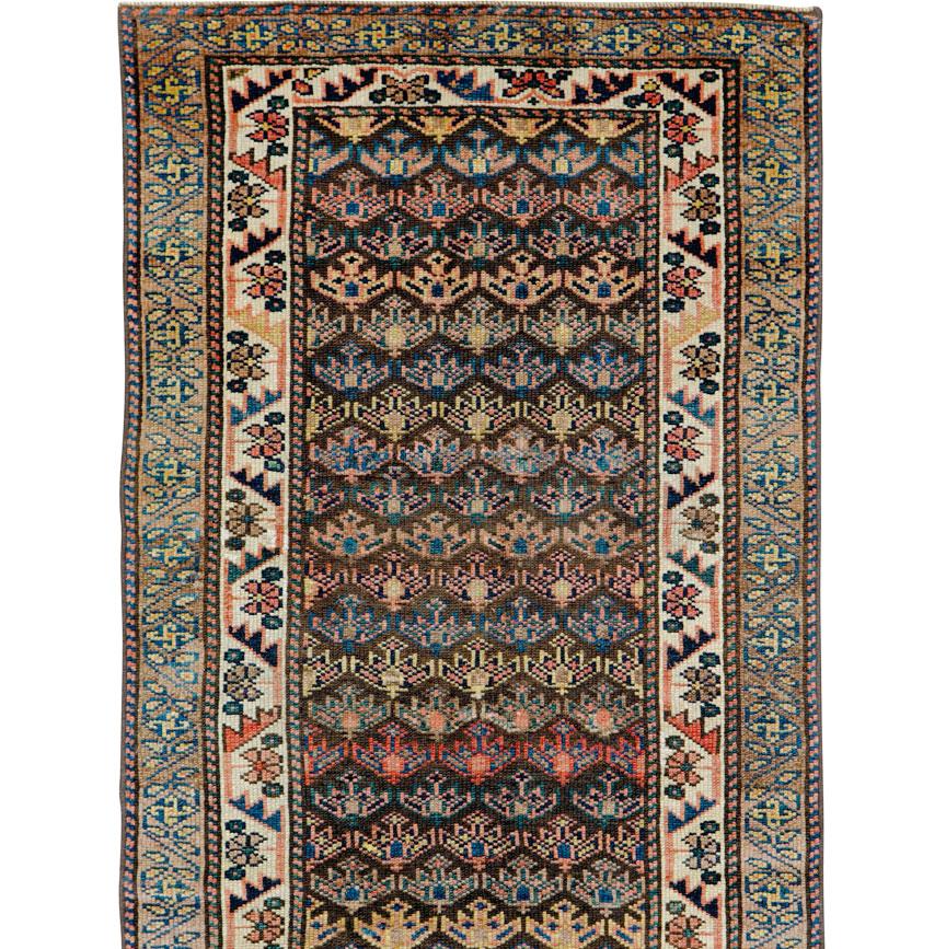 An antique Persian Kurdish runner from the early 20th century. Half-drop offset rows of unidirectional small, simple palmettes march up the charcoal and dark brown field of this west Persian Kurdish village small runner. Accents in medium blue,