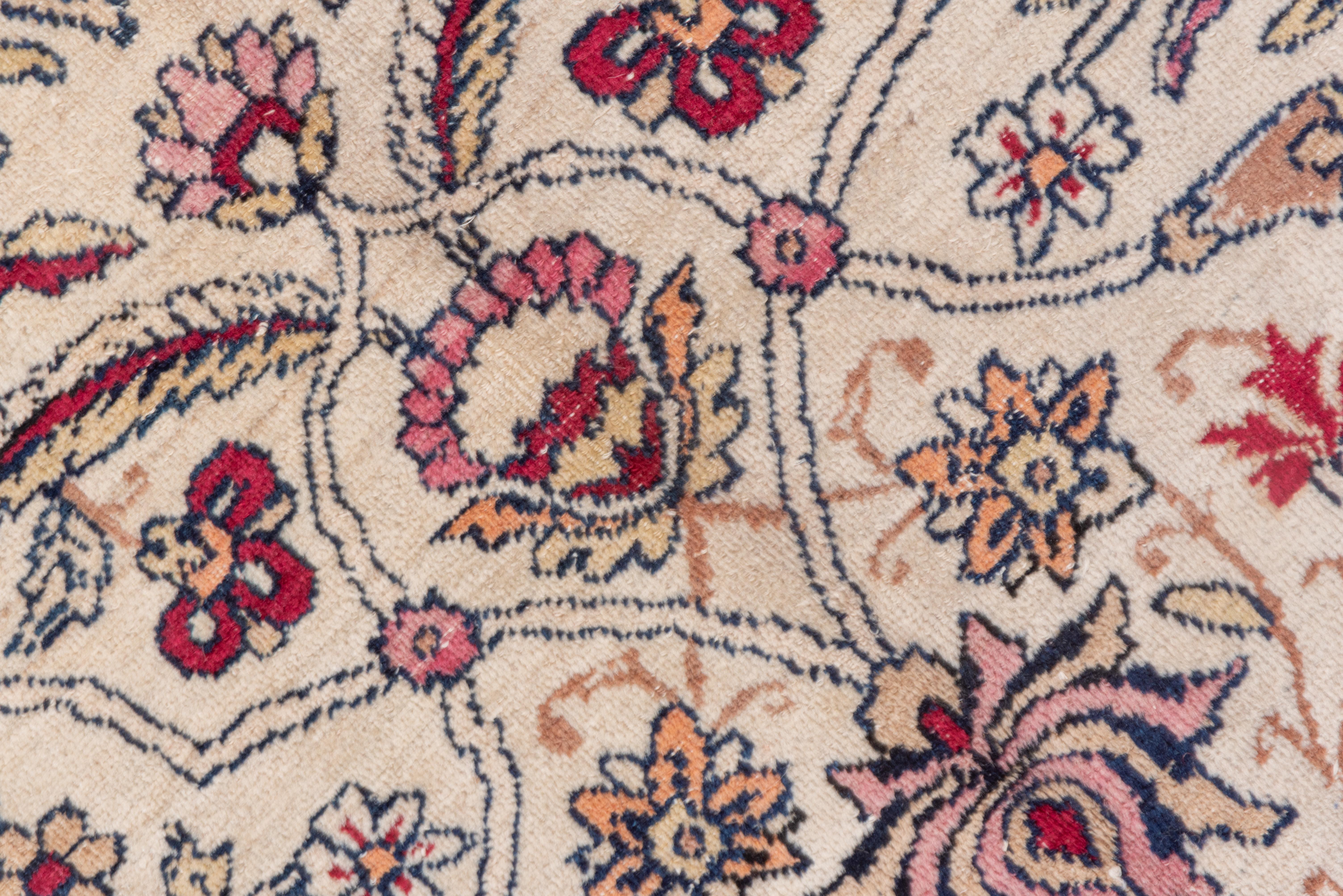 This well-woven SE Persian urban carpet presents an ecru field with an all-over pattern in three discrete columns of small medallions, palmettes, vinery in several levels and various garden flowers, with a wide light palette including soft teal,