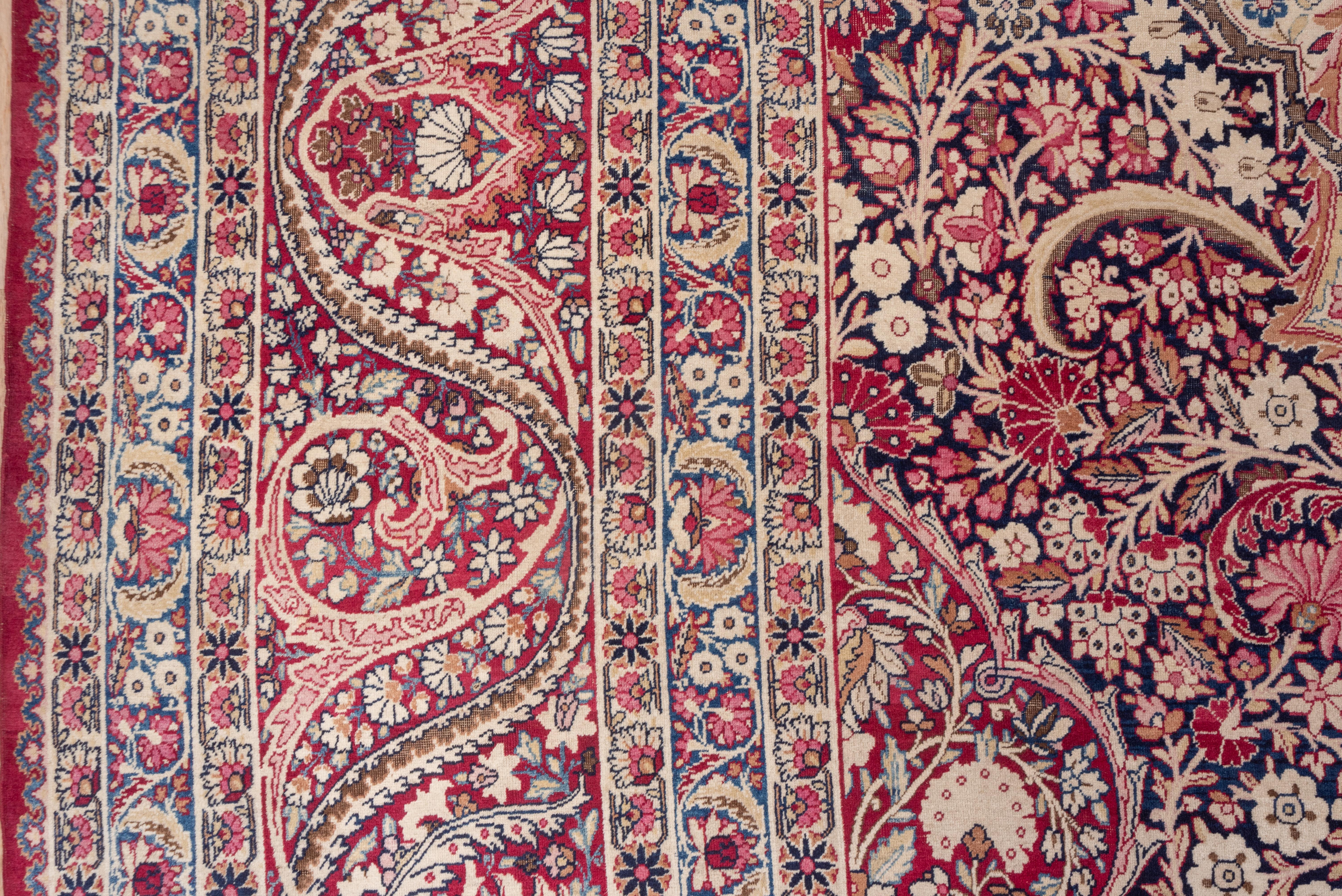 Lavar Kermans are of higher quality and this mansion carpet is an fine example with a navy field and wine red corners densely covered with a multi-layer vine and flower pattern supporting a 16-point palmette medallion. SE Persian Kerman city carpets