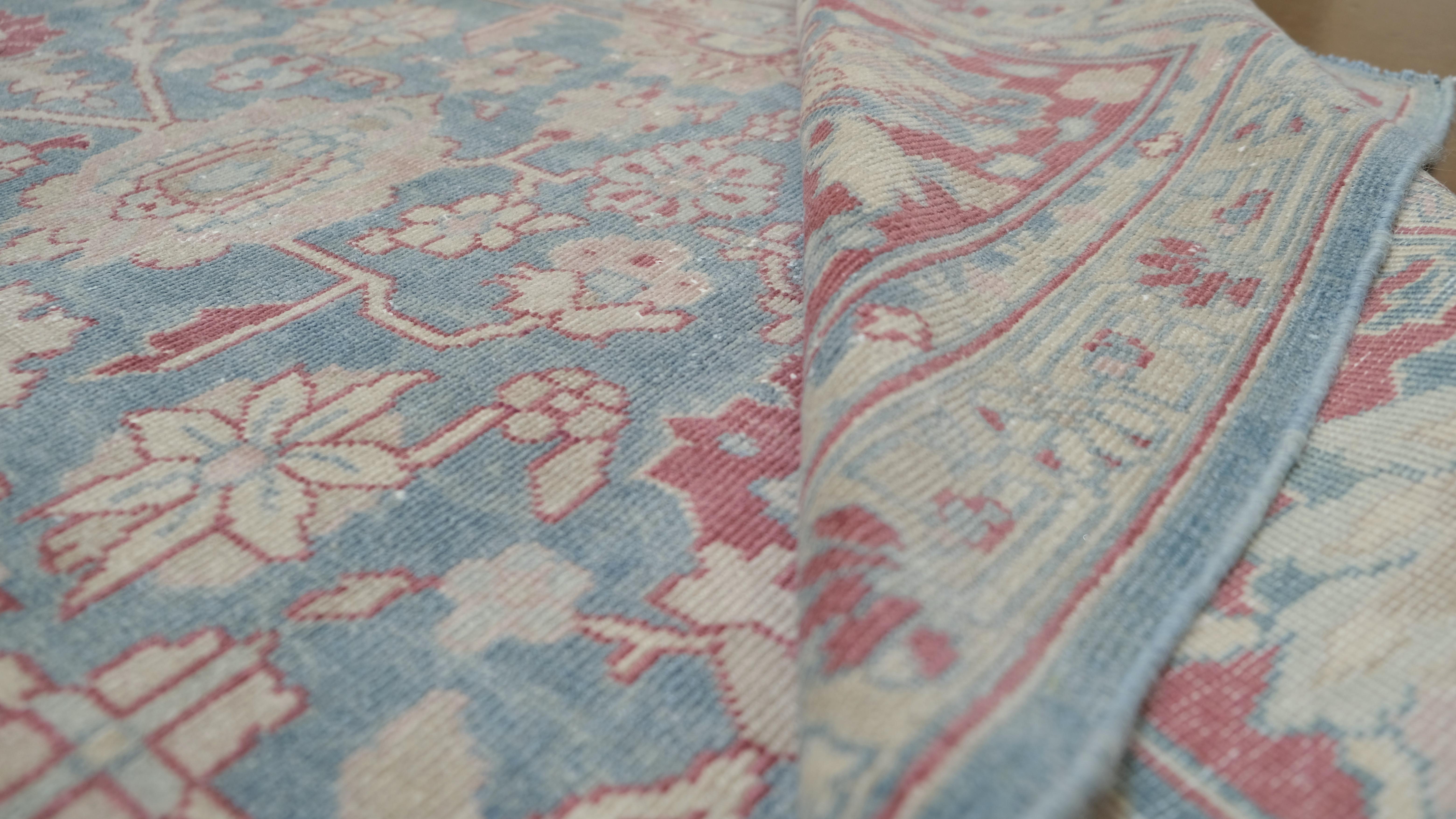 Dieser exquisite antike, handgeknüpfte Wollteppich zeigt ein atemberaubendes Blumenmuster auf einem ruhigen blauen Feld, eingerahmt von einer eleganten Bordüre mit verschlungenen botanischen Motiven. Die harmonische Mischung aus sanftem Blau,