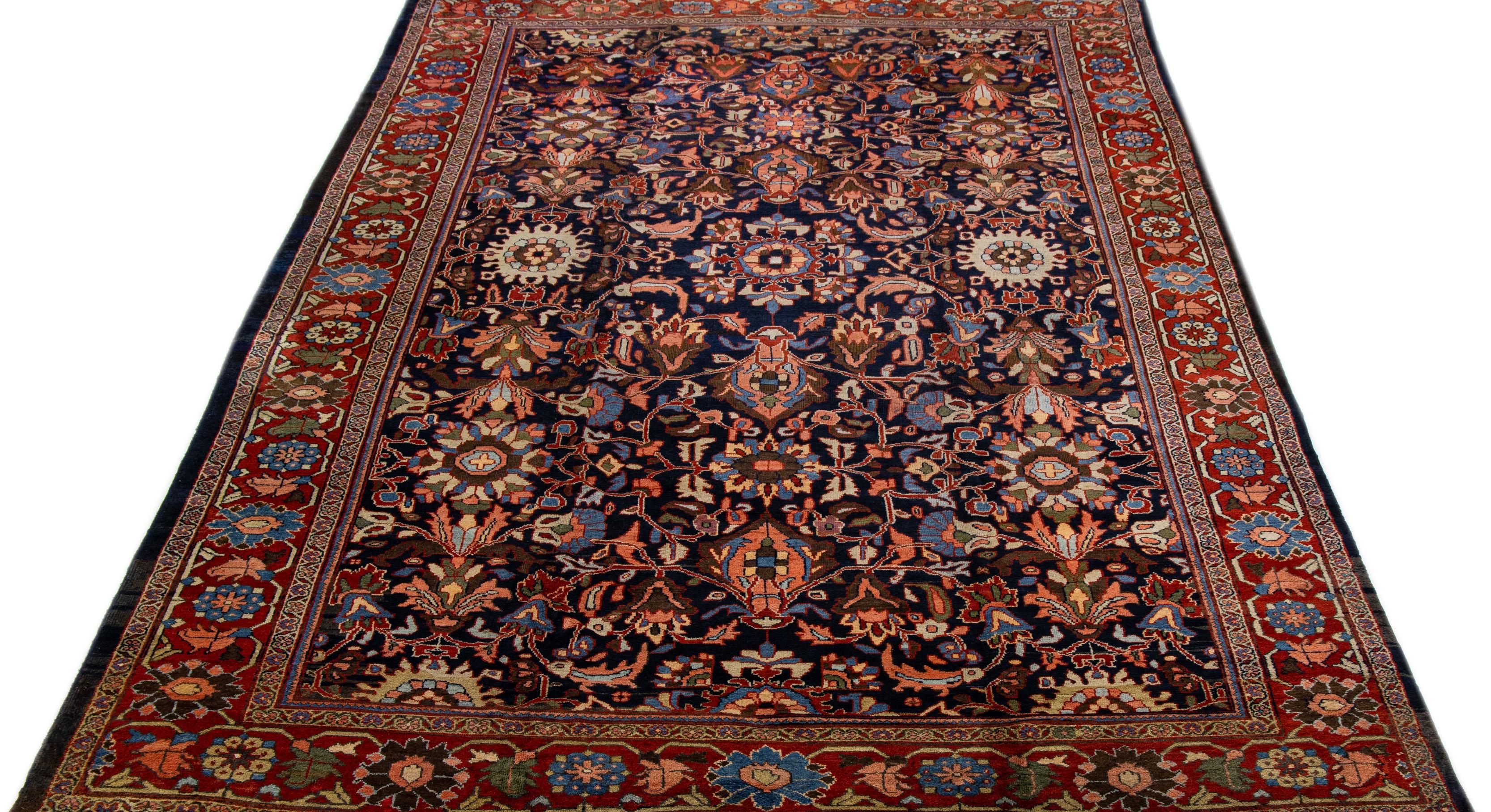 A stunning antique mahal wool rug, exquisitely hand knotted and endowed with a mesmerizing navy blue color field. This Persian masterpiece showcases a red designed frame that encases an all-over floral pattern, beautifully accentuated with