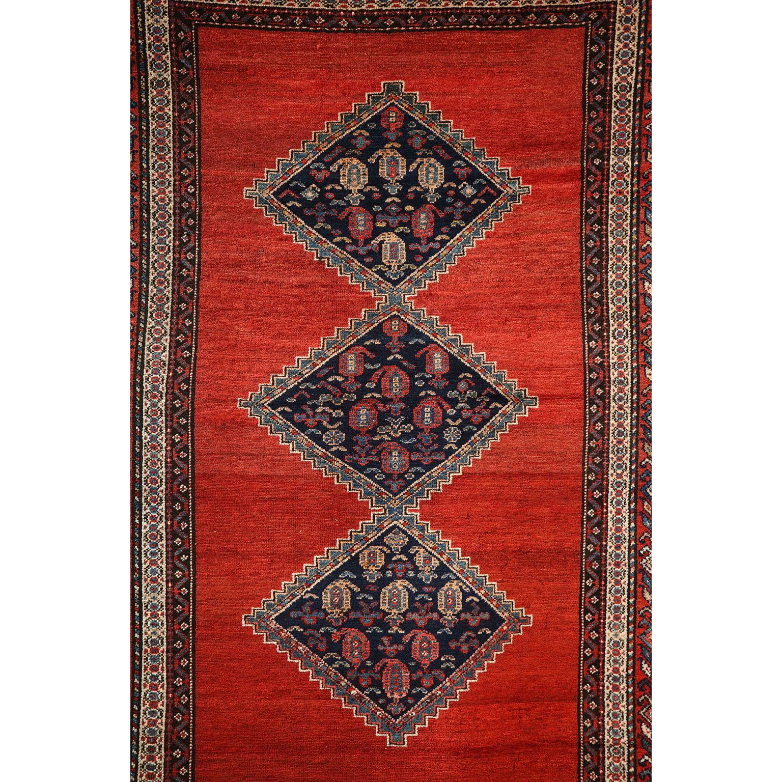 This antique Persian Malayer carpet in pure wool and vegetable dyes circa 1900 features a triple diamond central medallion with an intricate multiple band border and vibrant red field. Its organic coloration of vegetable dyed red and indigo creates