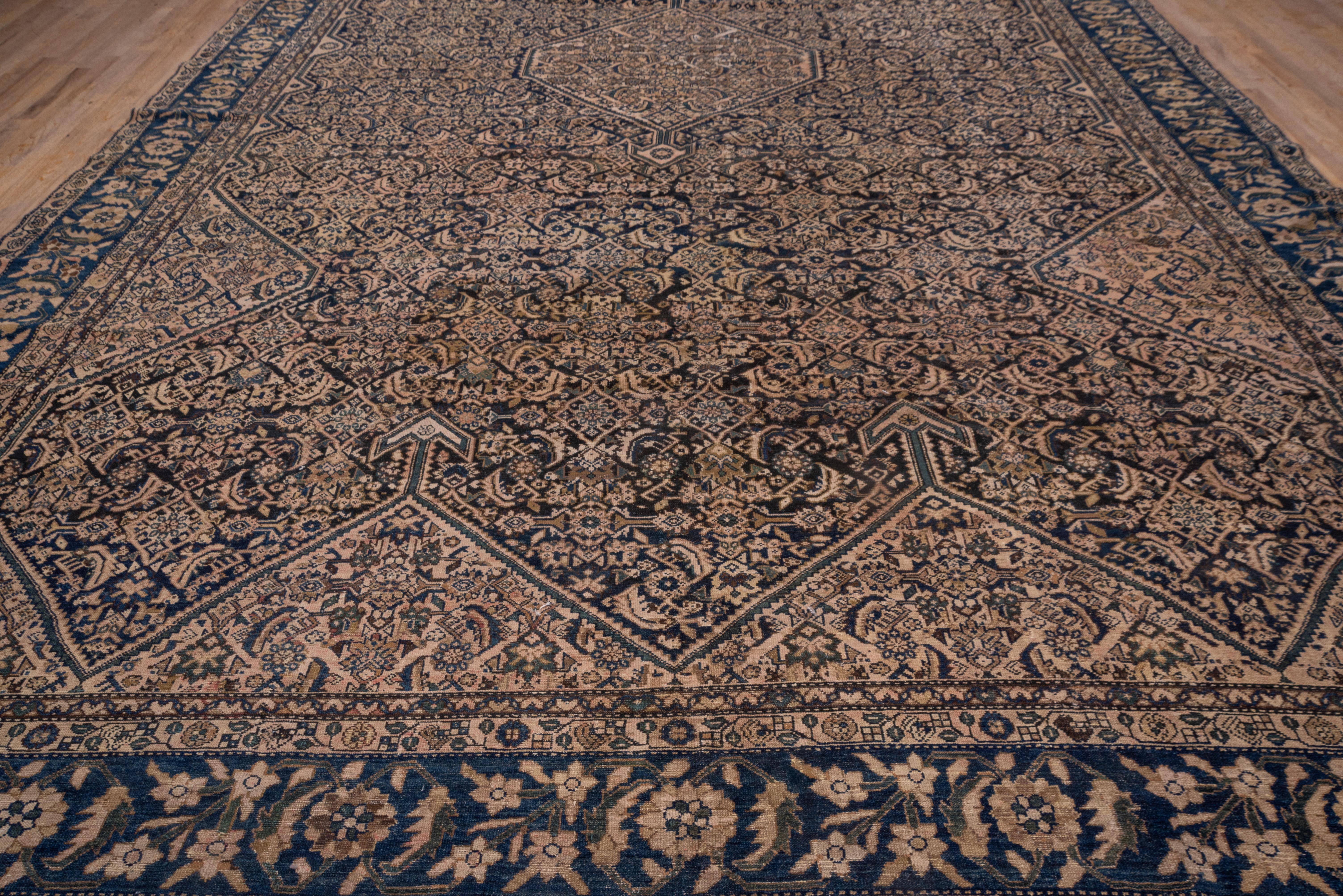 This west Persian village carpet is all Herati: in the pendanted, ivory hexagonal medallion, the end and side cream sections, and in the dark blue shaped sub field. The dark blue border presents a version of the tangerine flower repeat with