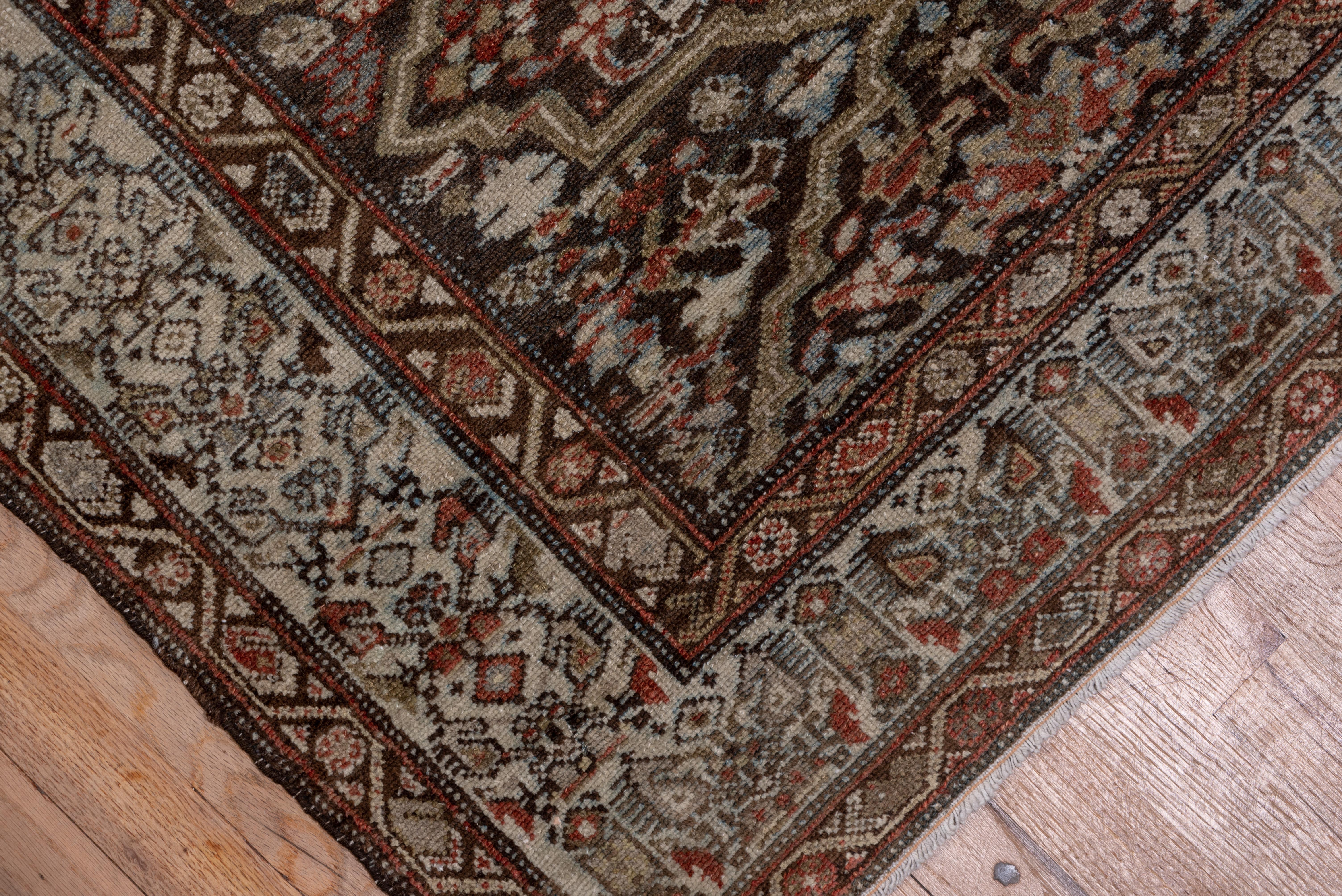 This West Persian runner shows 15 whole barbed lozenge cartouches forming a central pole, each enclosing a rosette, on a dark slate ground, with red, green and ecru accents. Straw border with a unidirectional, modular footed boteh repeat.
