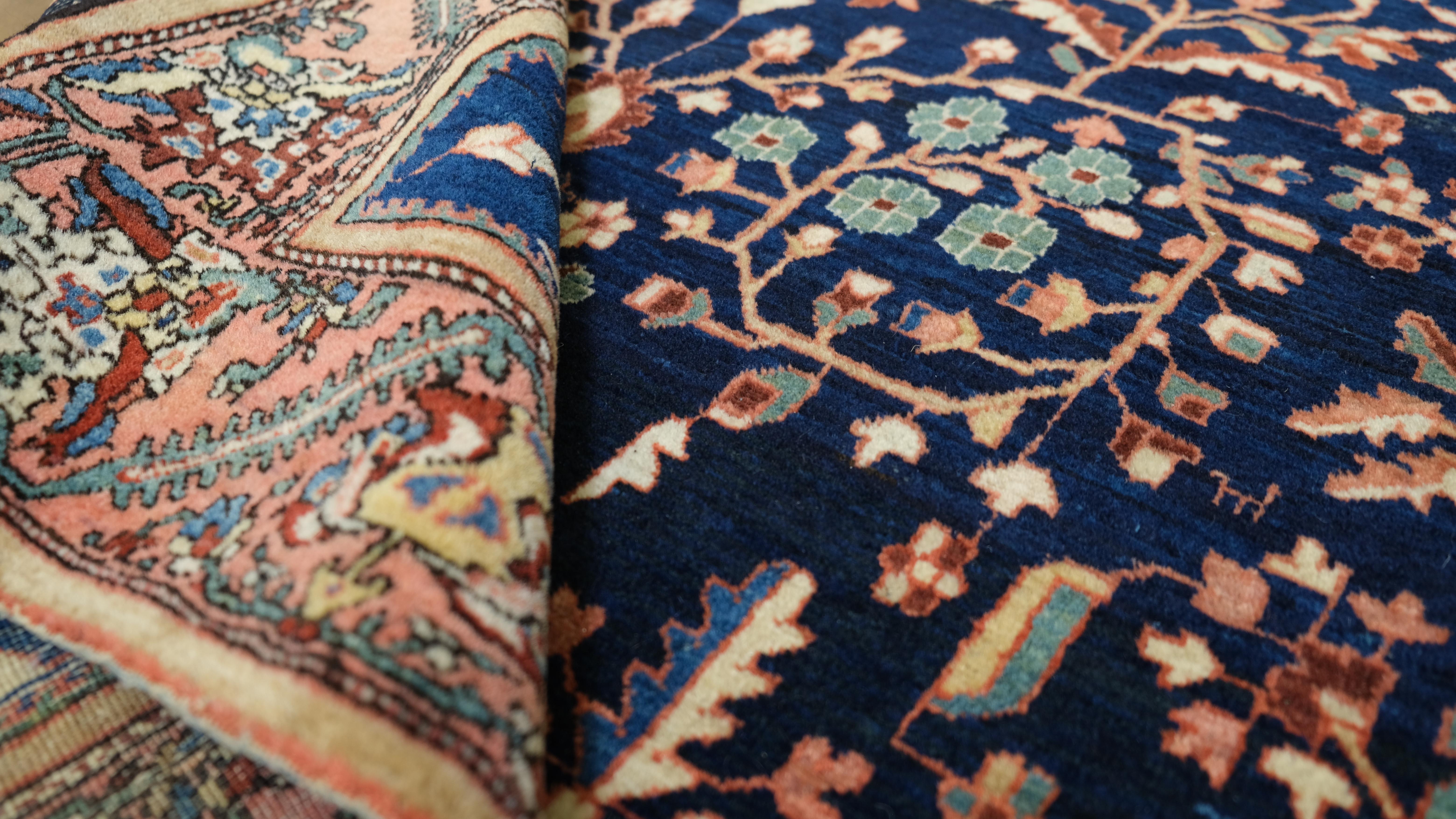 This exquisite antique hand-knotted wool rug showcases a breathtaking Tree of Life floral design, set against a deep navy blue background with intricate botanical motifs in coral, ivory, and teal. The rug’s symmetrical composition features