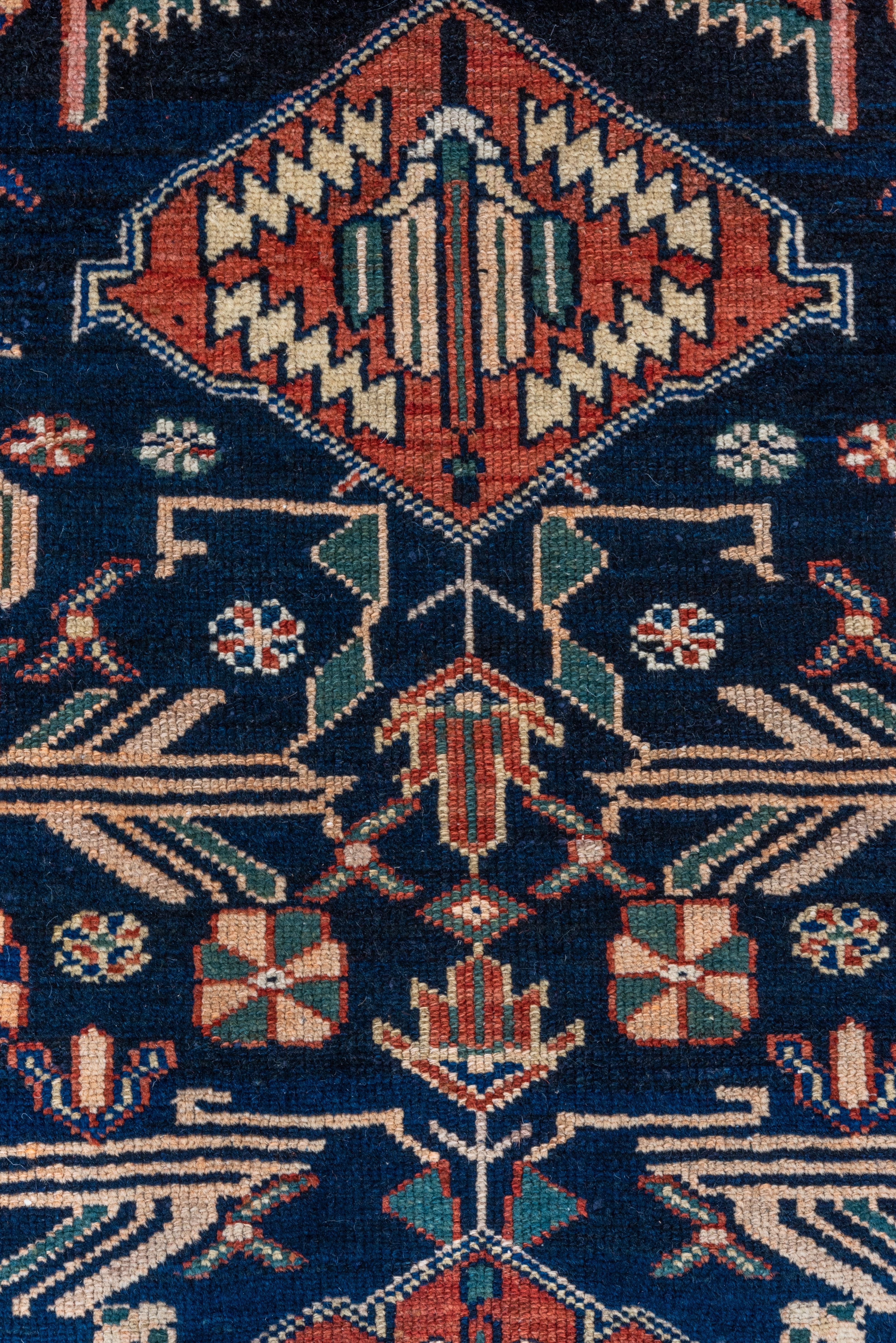 The royal blue field displays two converging modules with paired saw tooth , finial striated palmettes and rust flattened hexagons, with stylised flowers and stems around, detailed in teal and sand. Royal blue border in the Kurdish 