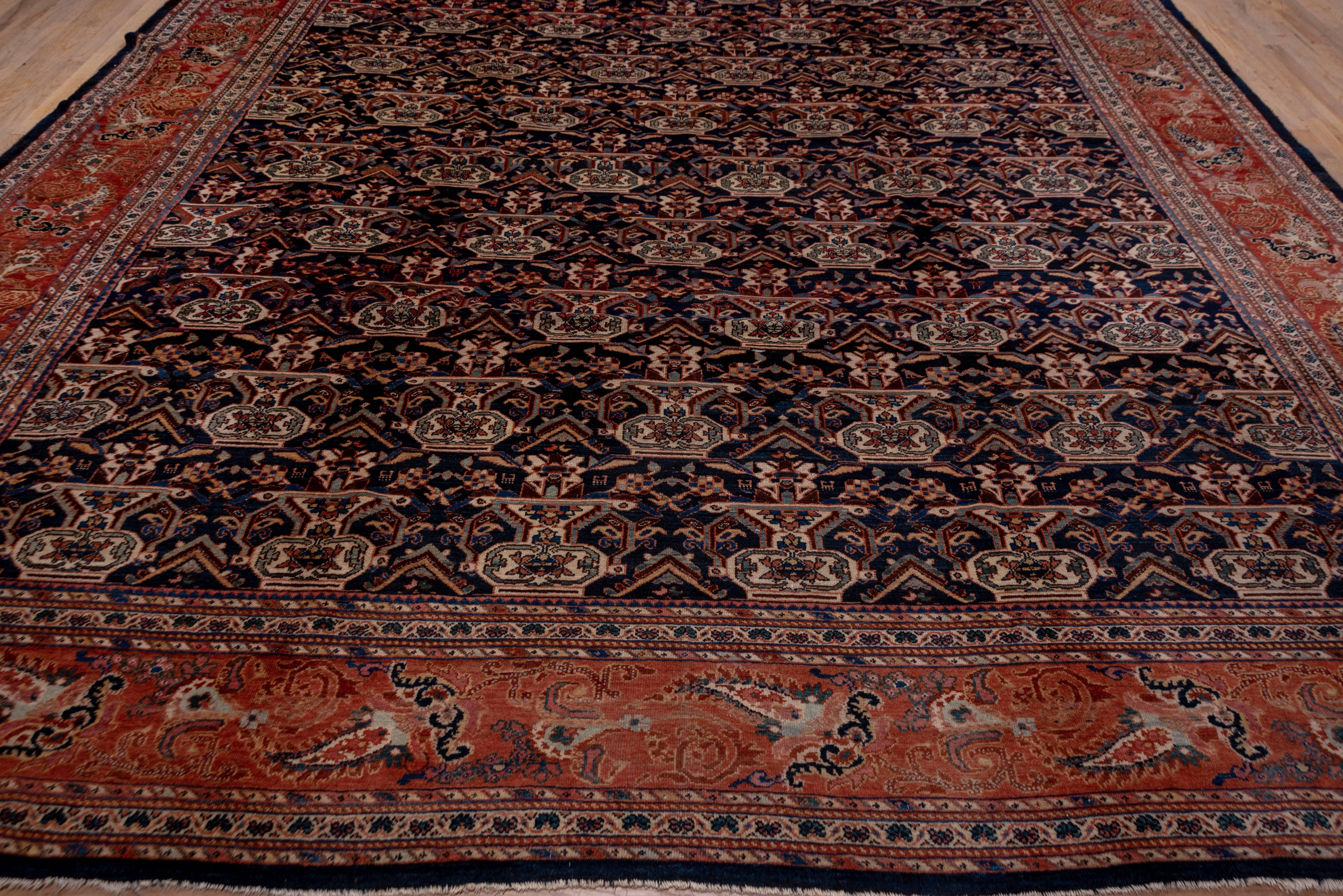 This top condition, full pile western Persian town carpet displays an unusual staggered row vase design on a dark blue ground with details in ivory, green and goldenrod. He rust border shows floriated bottehs derived from European printed textiles.